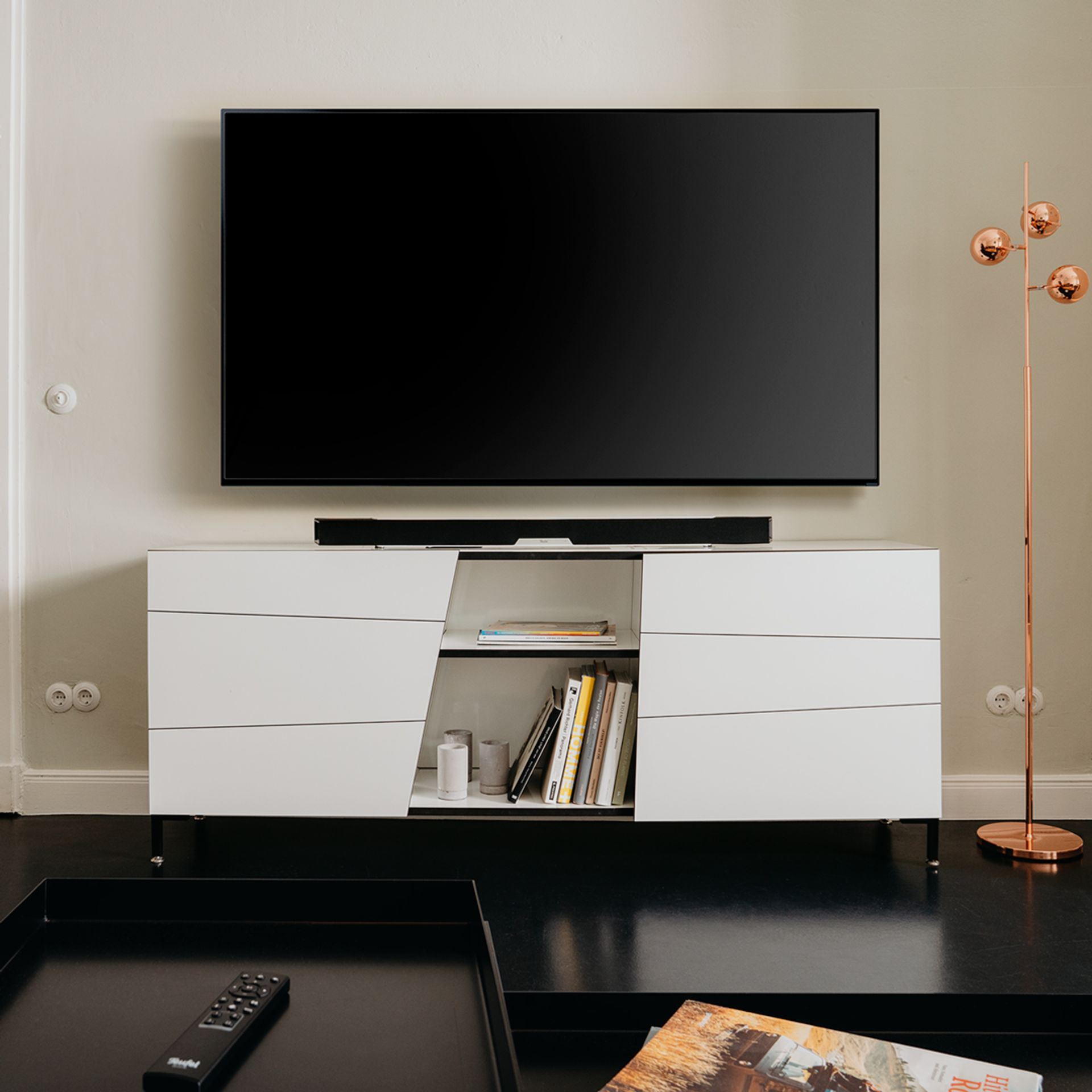 Ein moderner weißer Schrank mit Fernseher und Soundbar. Bücher und Deko stehen im Regal.