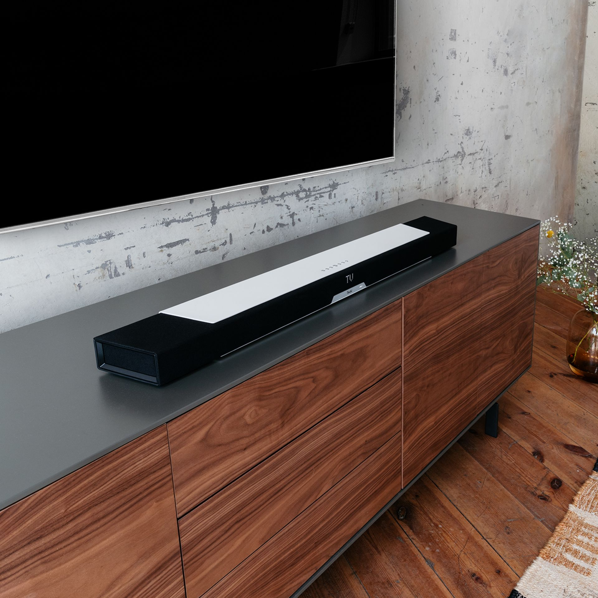 Eine schwarz-weiße Soundbar auf einem Holzschrank unter einem großen Fernsehbildschirm.