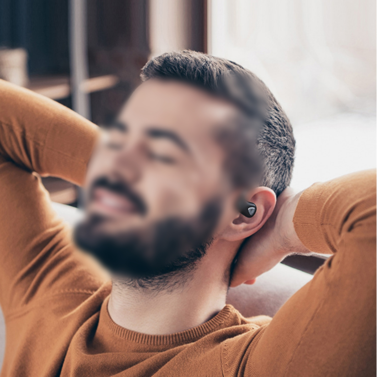 Mann mit orangefarbenem Pullover und schwarzem Ohrhörer. Der Hintergrund ist unscharf.