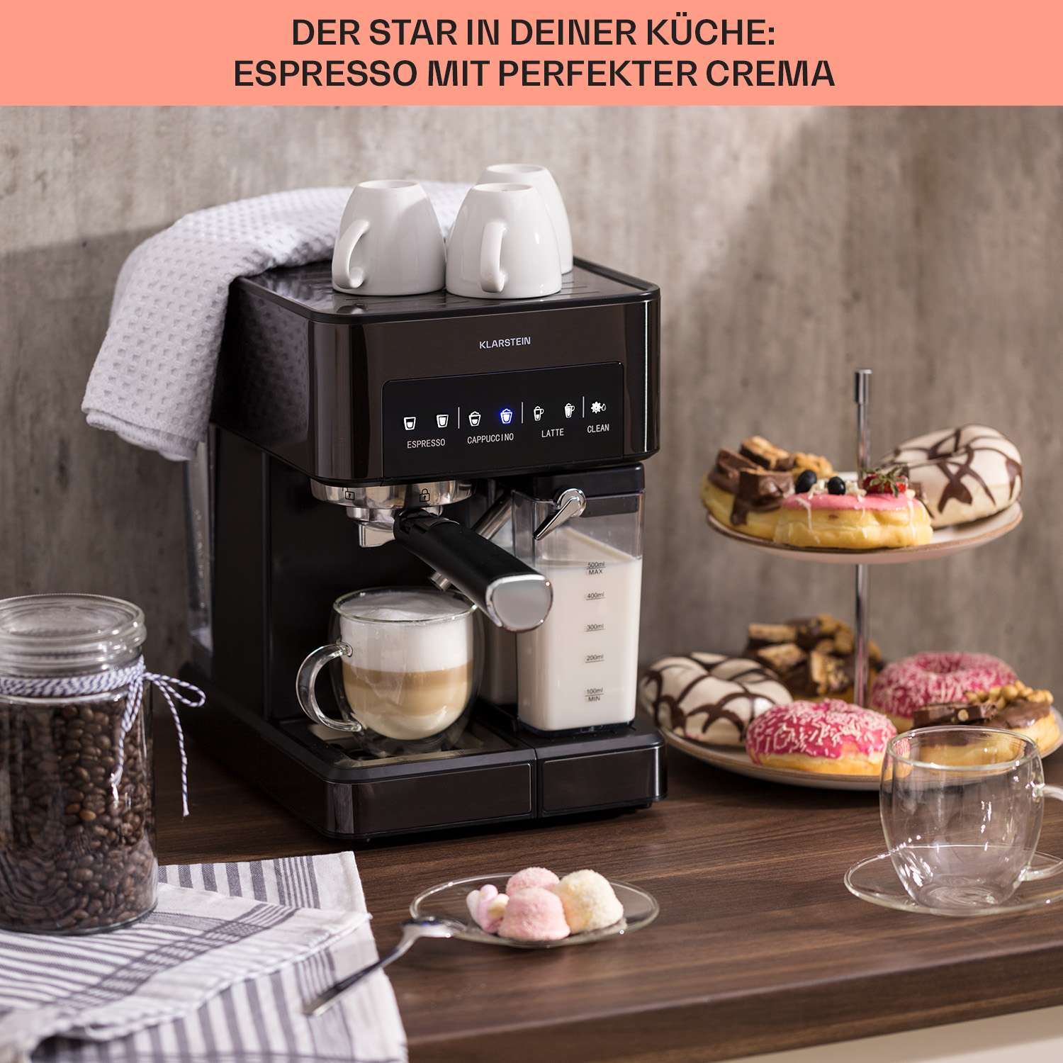 Máquina de espresso negra con taza. Donas en soporte, granos de café en tarro de vidrio.