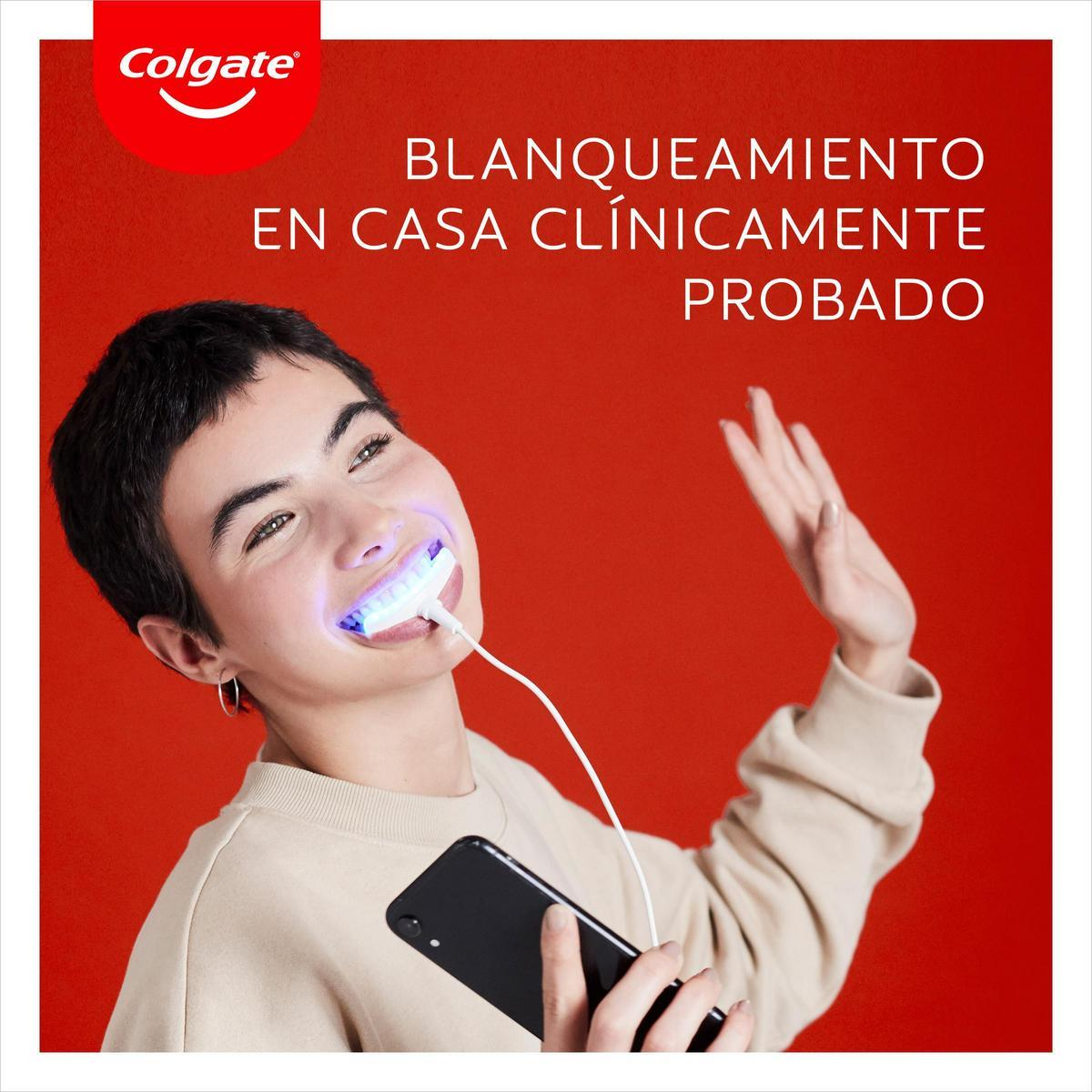Una mujer usando un dispositivo de blanqueamiento dental, sosteniendo un teléfono negro, con el logo de Colgate en el fondo.