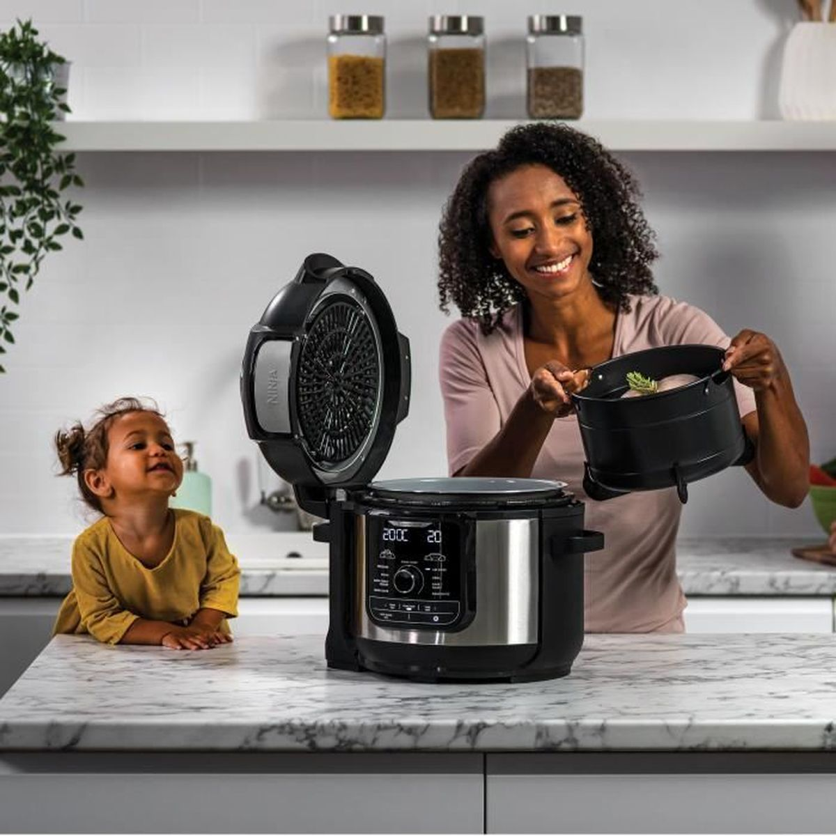 A woman and a child near a kitchen appliance. The woman is holding a black pot.
