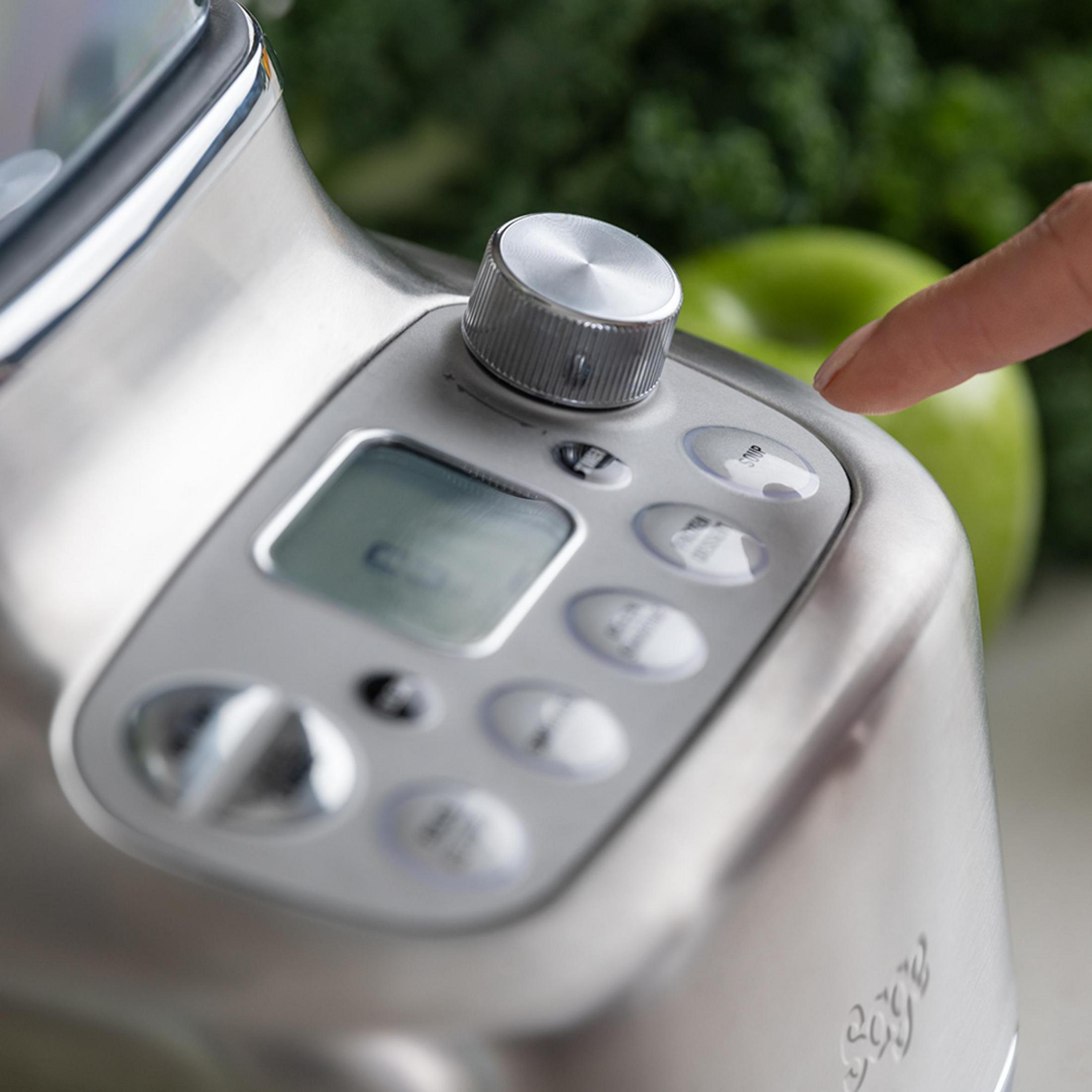 Srebrny blender z palcem naciskającym przycisk w pobliżu zielonego jabłka.