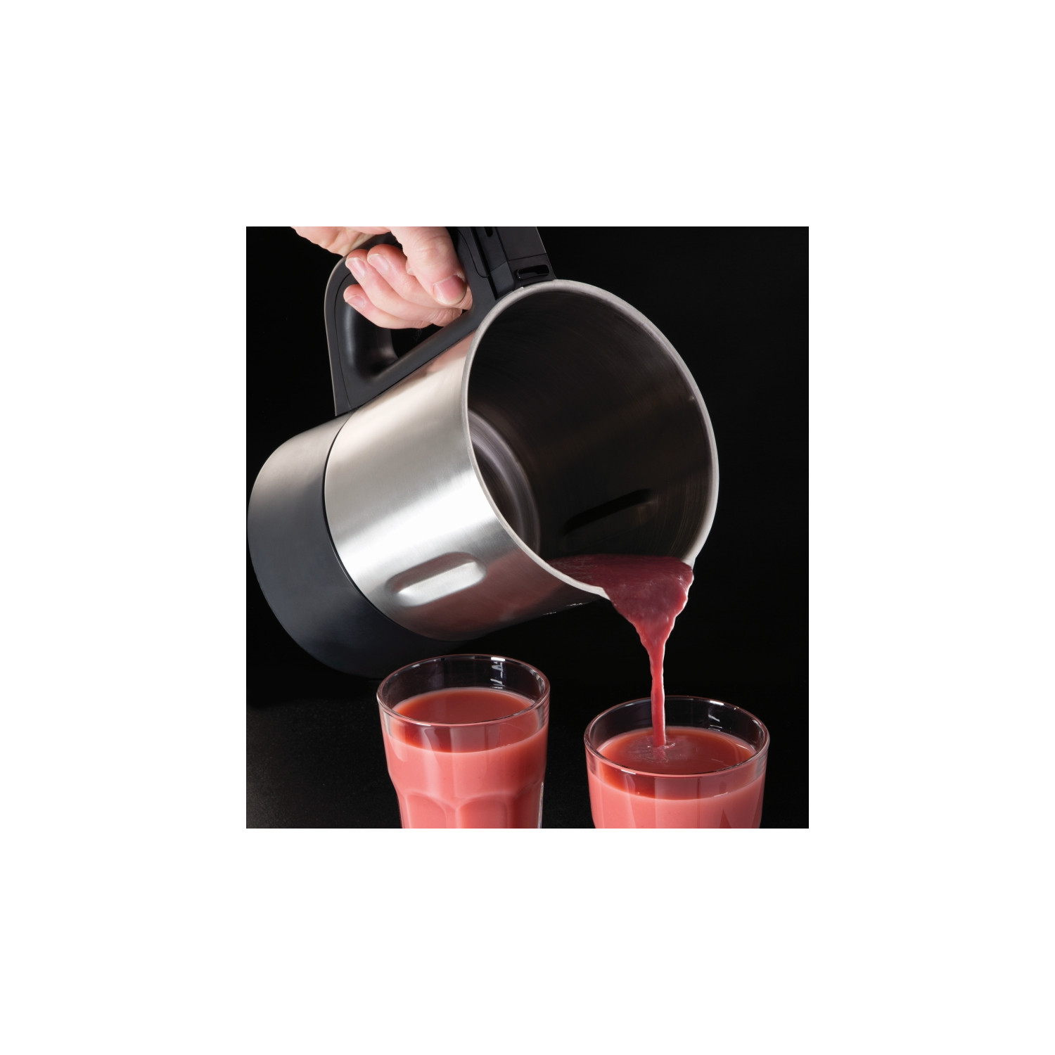 Un mélangeur en acier inoxydable verse du liquide rose dans deux verres transparents sur une surface noire.