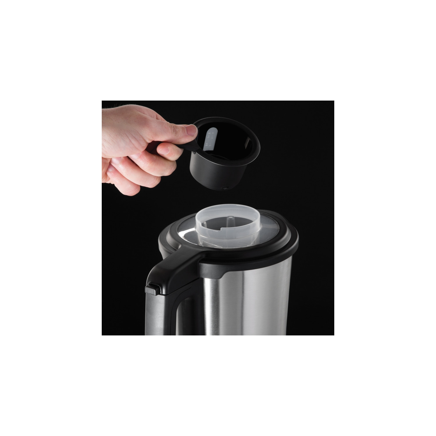 Personne versant une substance dans une cafetière en acier inoxydable. Poignée et couvercle noirs.