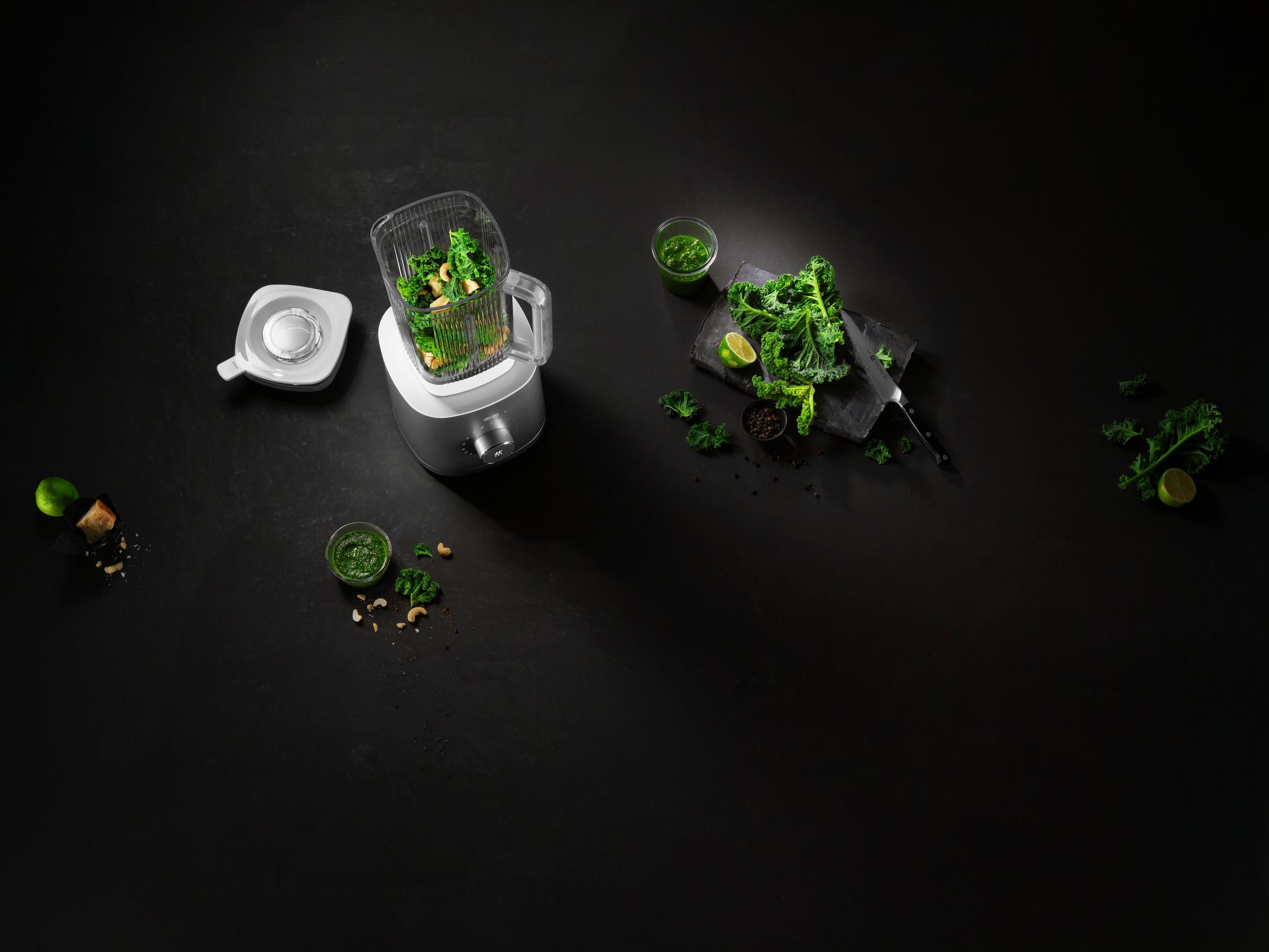 Blender z jarmużem, warzywami i składnikami na czarnej powierzchni do przepisu.