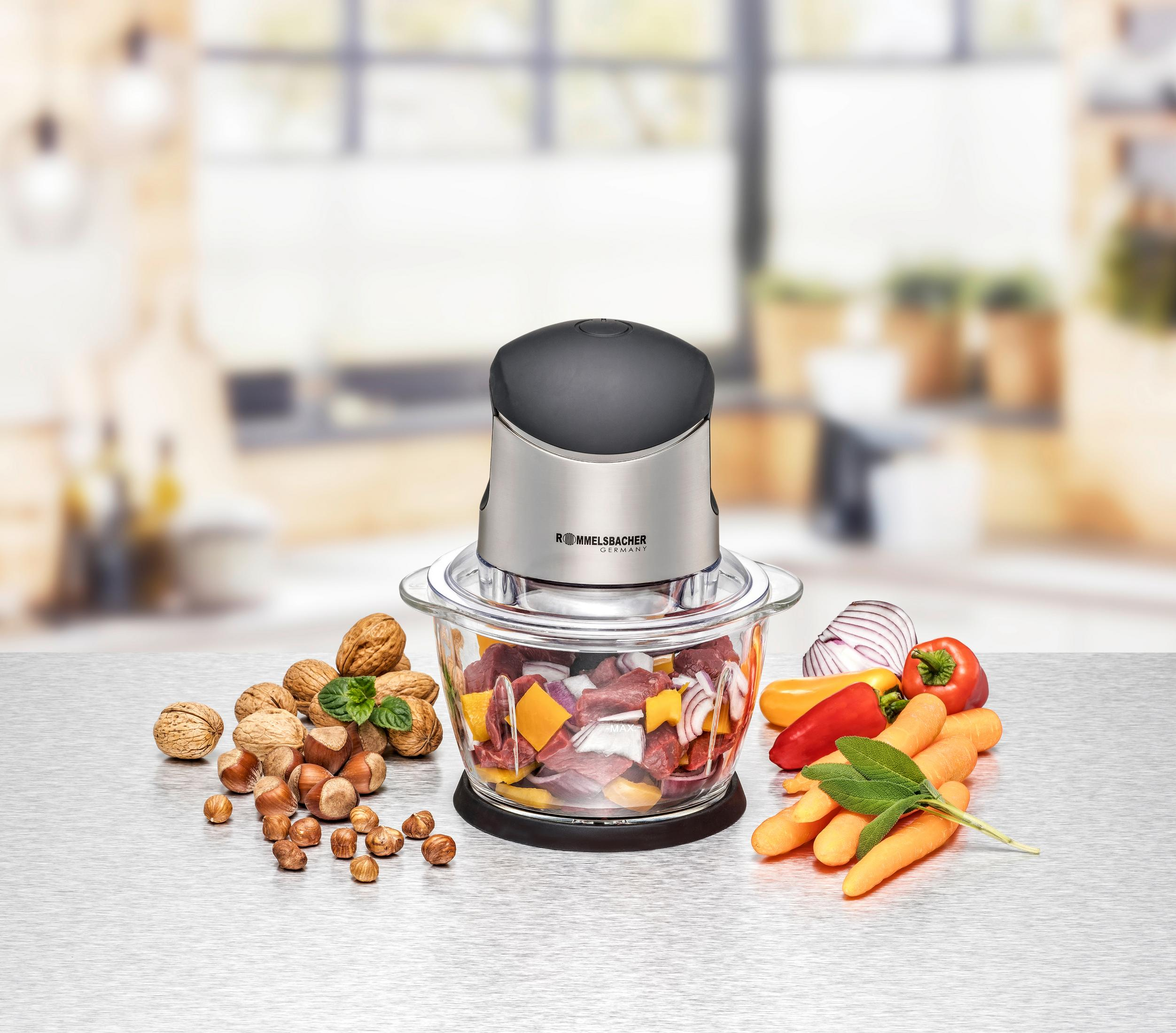 Un robot da cucina con ingredienti: noci, nocciole, carote, cipolle e pomodori su una superficie.