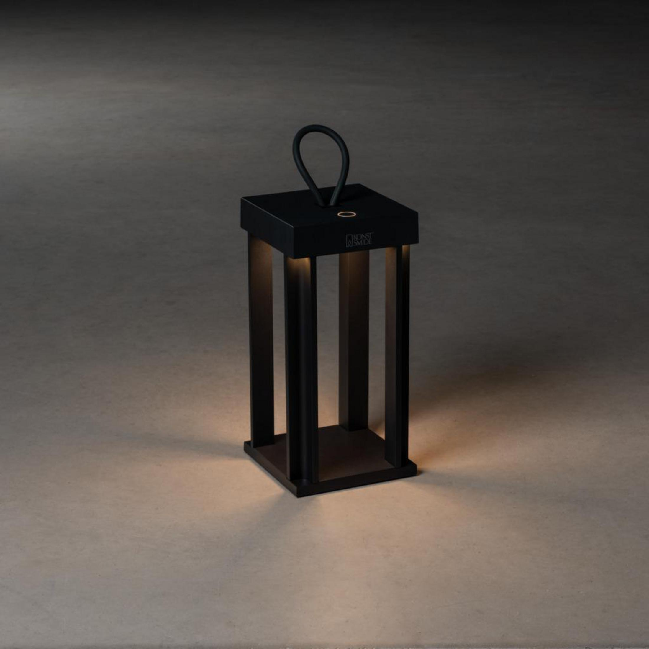 Eine schwarze Laterne hat einen Griff, und ein Licht beleuchtet ihren Sockel.