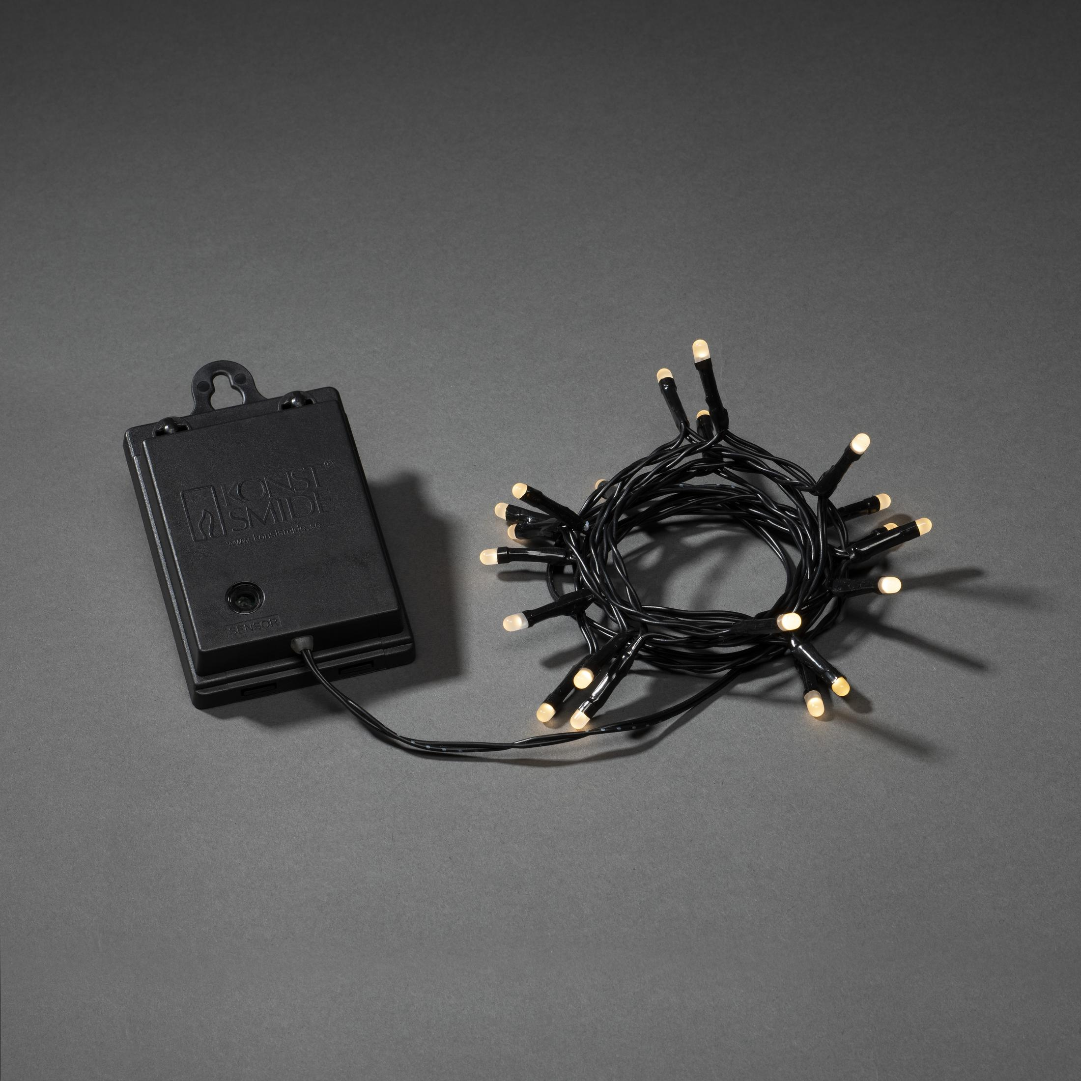 Eine Lichterkette und eine schwarze Box. Die Lichter sind weiß und die Box ist mit Text beschriftet.