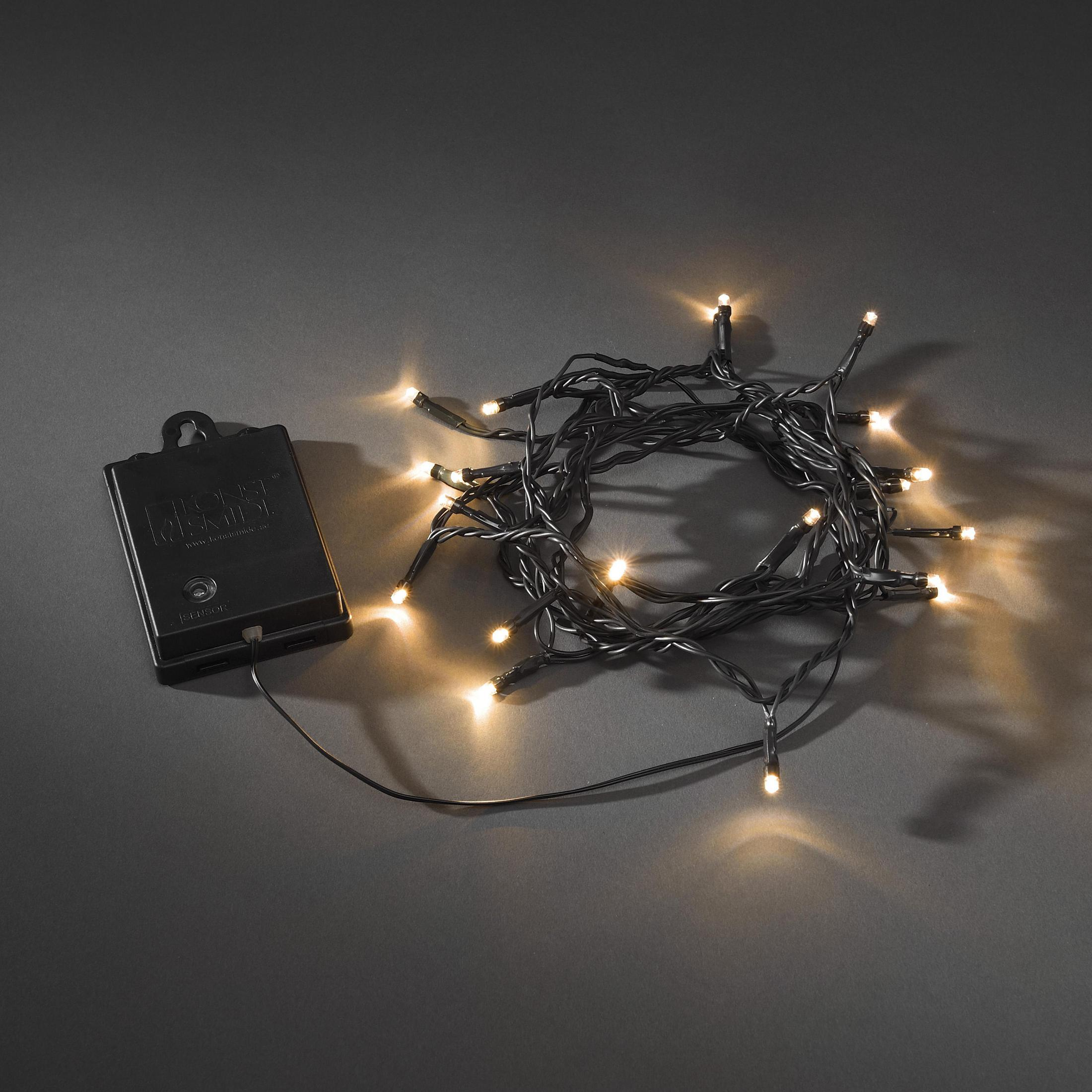 Lichterkette und ein schwarzes Batteriepack auf grauer Oberfläche. Die Lichter sind an.