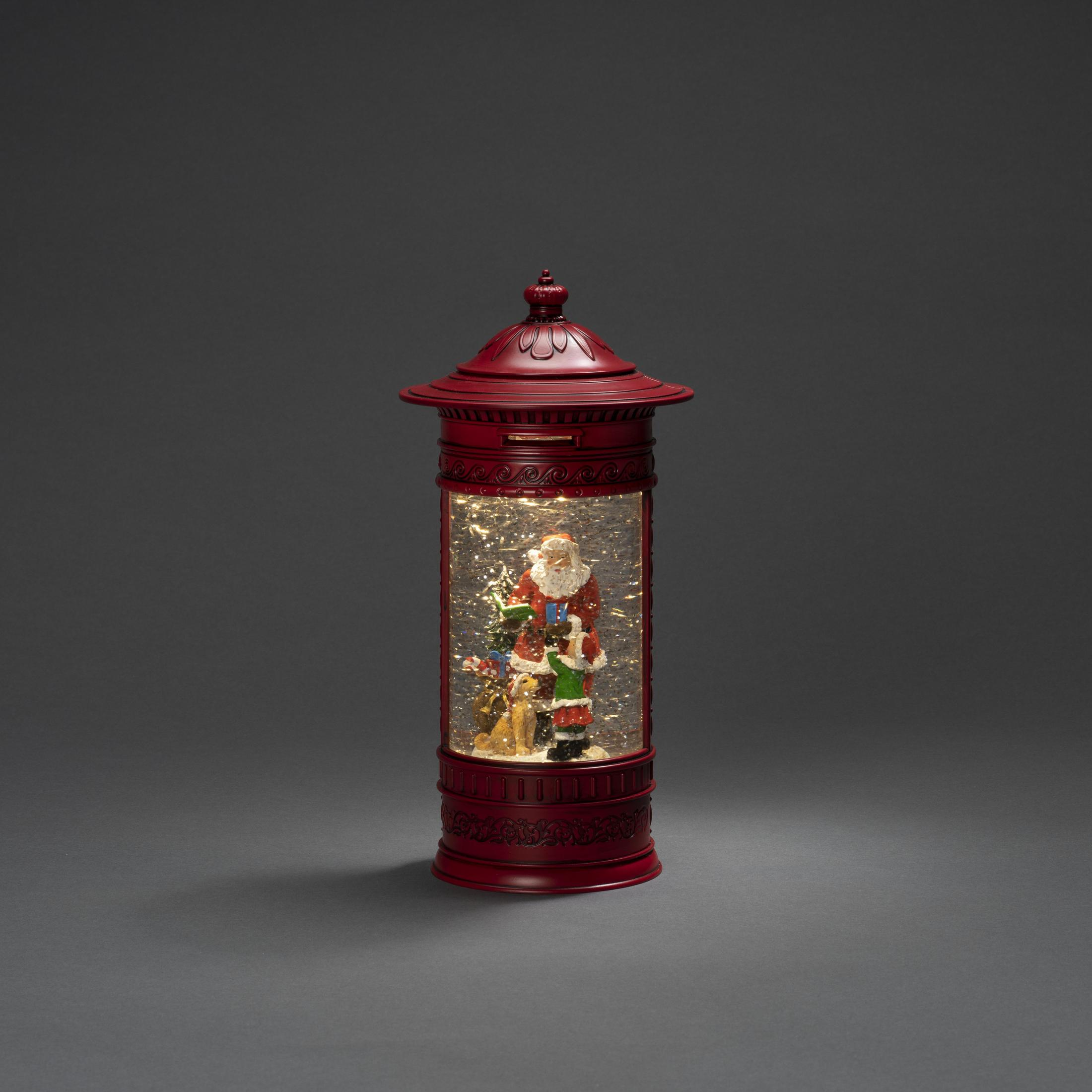 Eine rote Schneekugel mit einem Weihnachtsmann und Figuren darin. Sie steht auf einem dunkelgrauen Hintergrund.