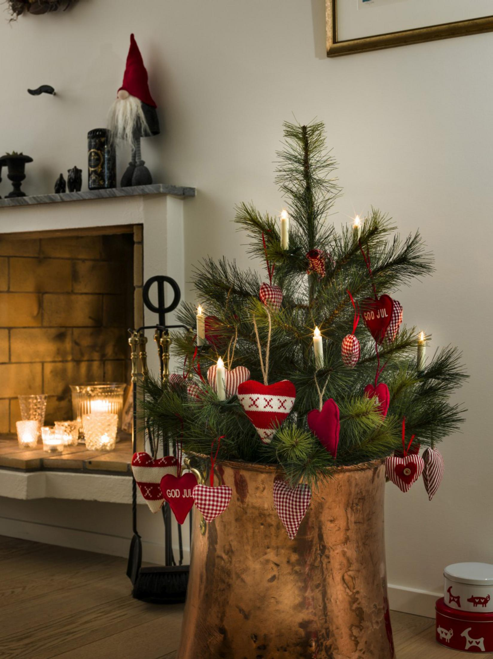 Ein Weihnachtsbaum in einem Kupfertopf, mit Herzschmuck und brennenden Kerzen.