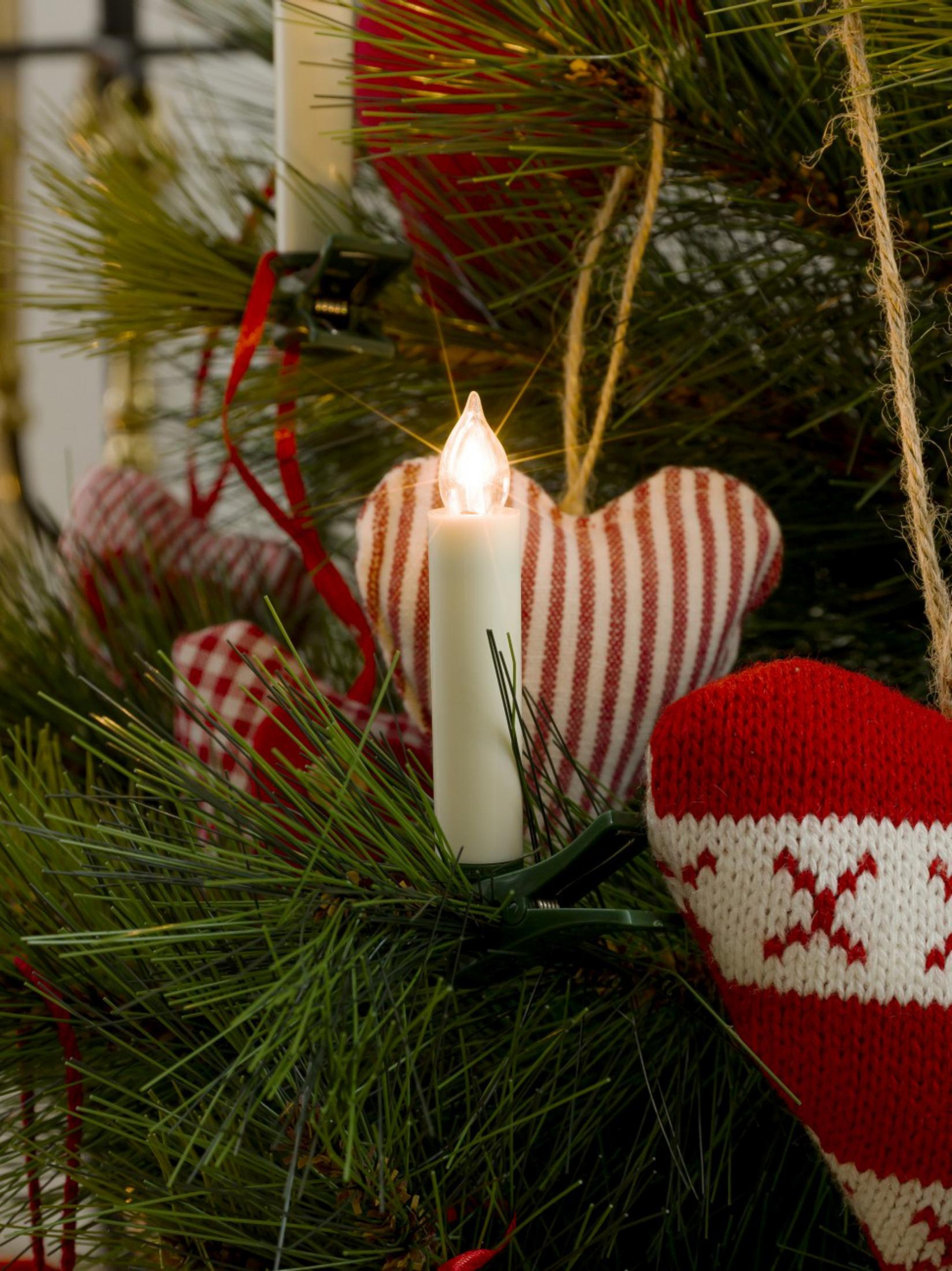 Ein Weihnachtsbaumzweig mit einer brennenden Kerze, roten Herzornamenten und anderen Dekorationen.