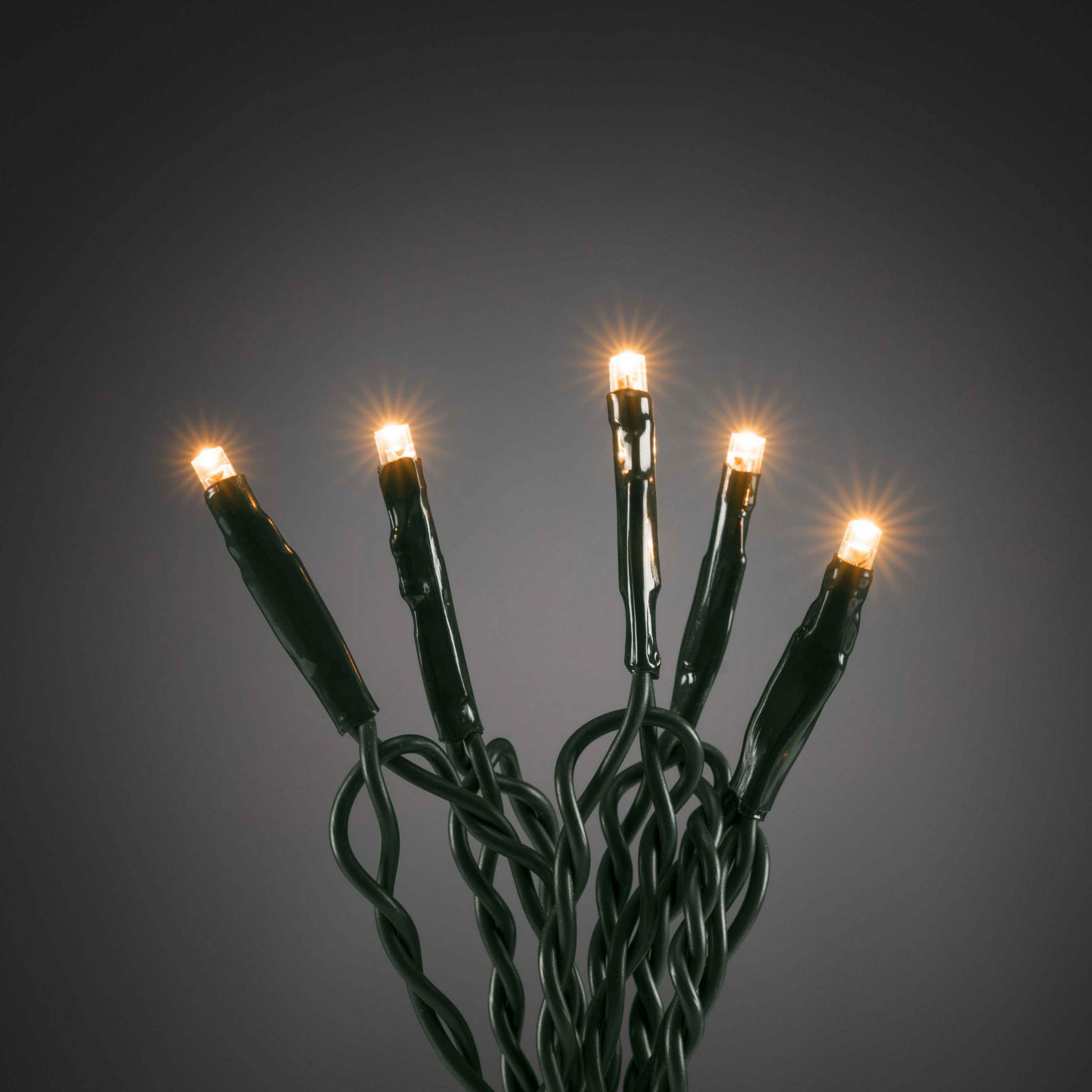 Primo piano di luci a stringa verdi con cinque luci arancioni luminose su sfondo scuro.