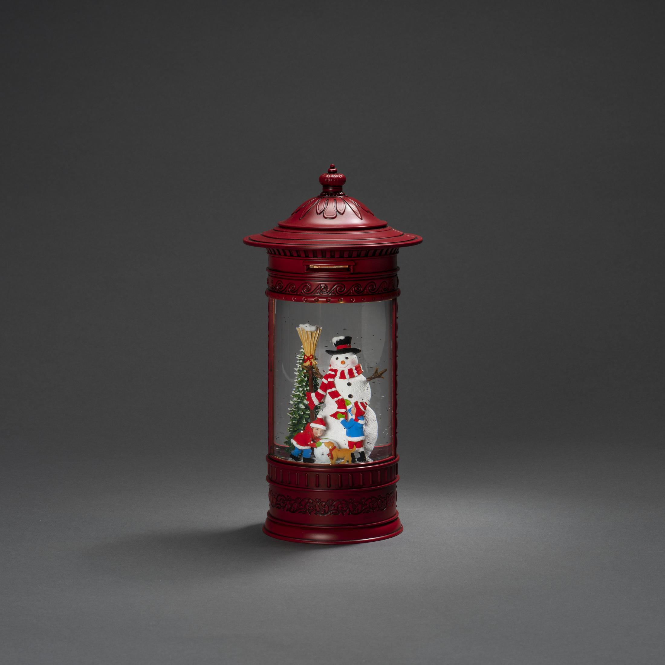Eine rote Schneekugel mit einem Schneemann und Figuren darin. Sie steht auf einem dunkelgrauen Hintergrund.