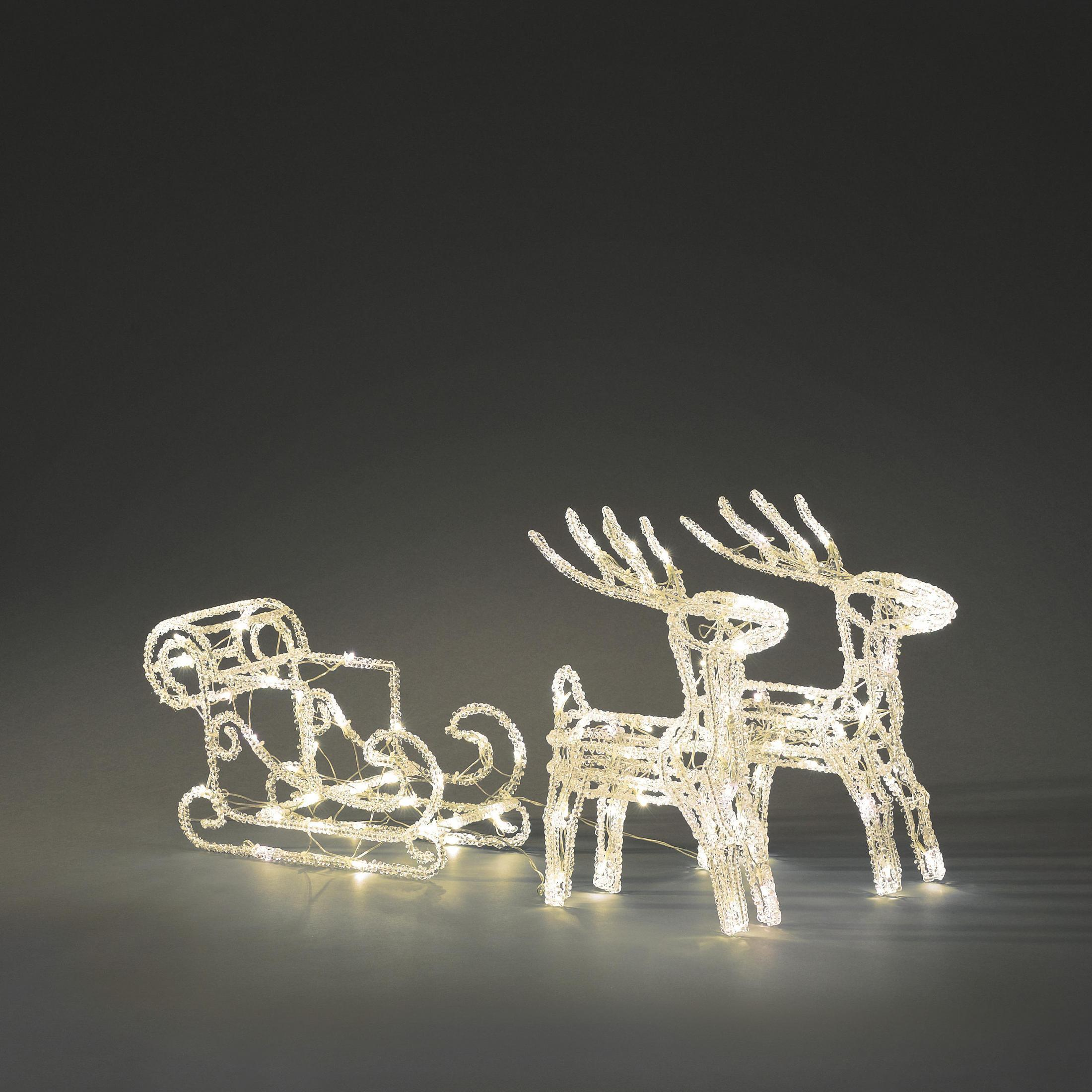 Decorazioni natalizie di renne e slitte, illuminate con luci bianche, su sfondo grigio.
