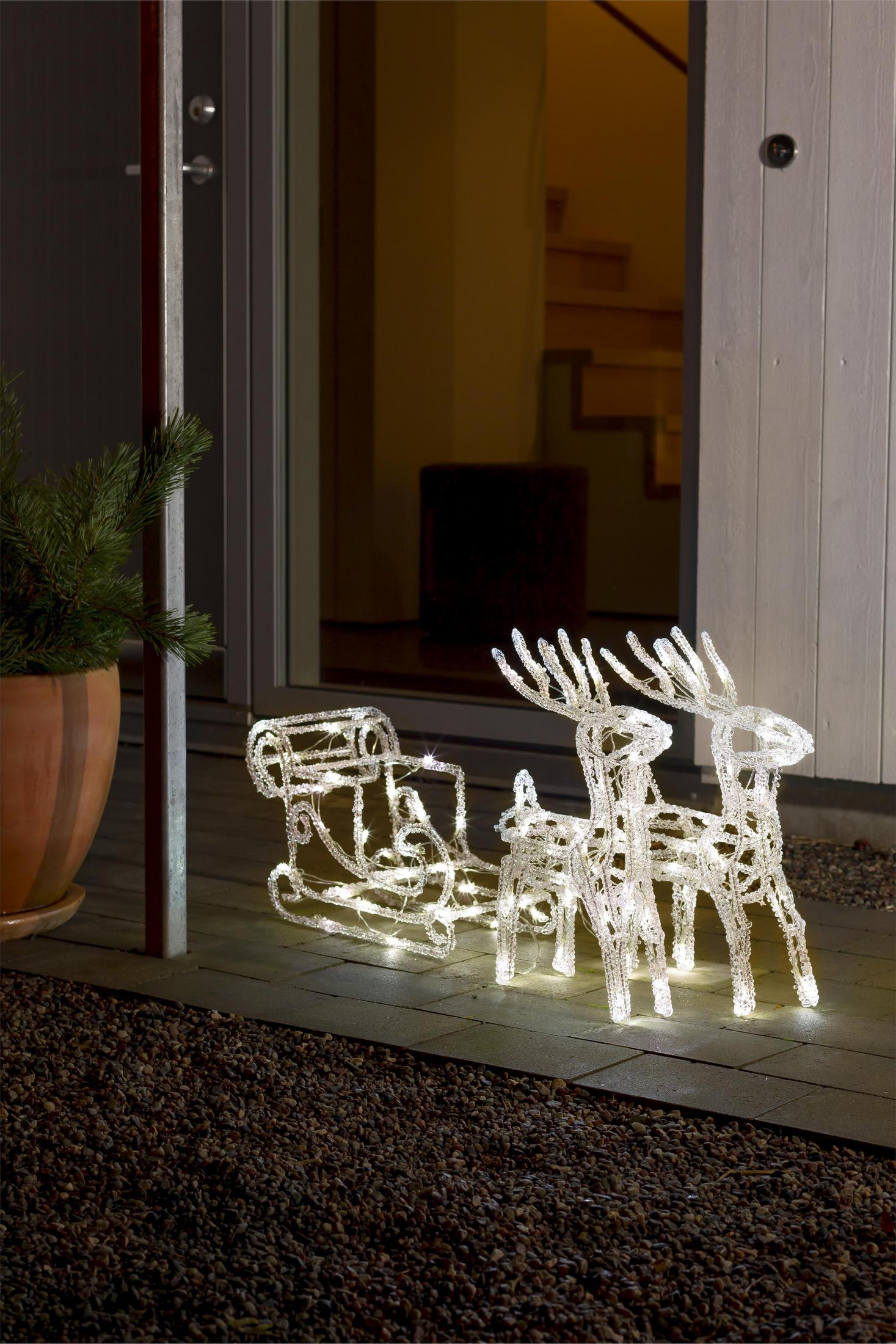 Decorazioni natalizie: renne illuminate e una slitta su un patio, vicino a una casa.
