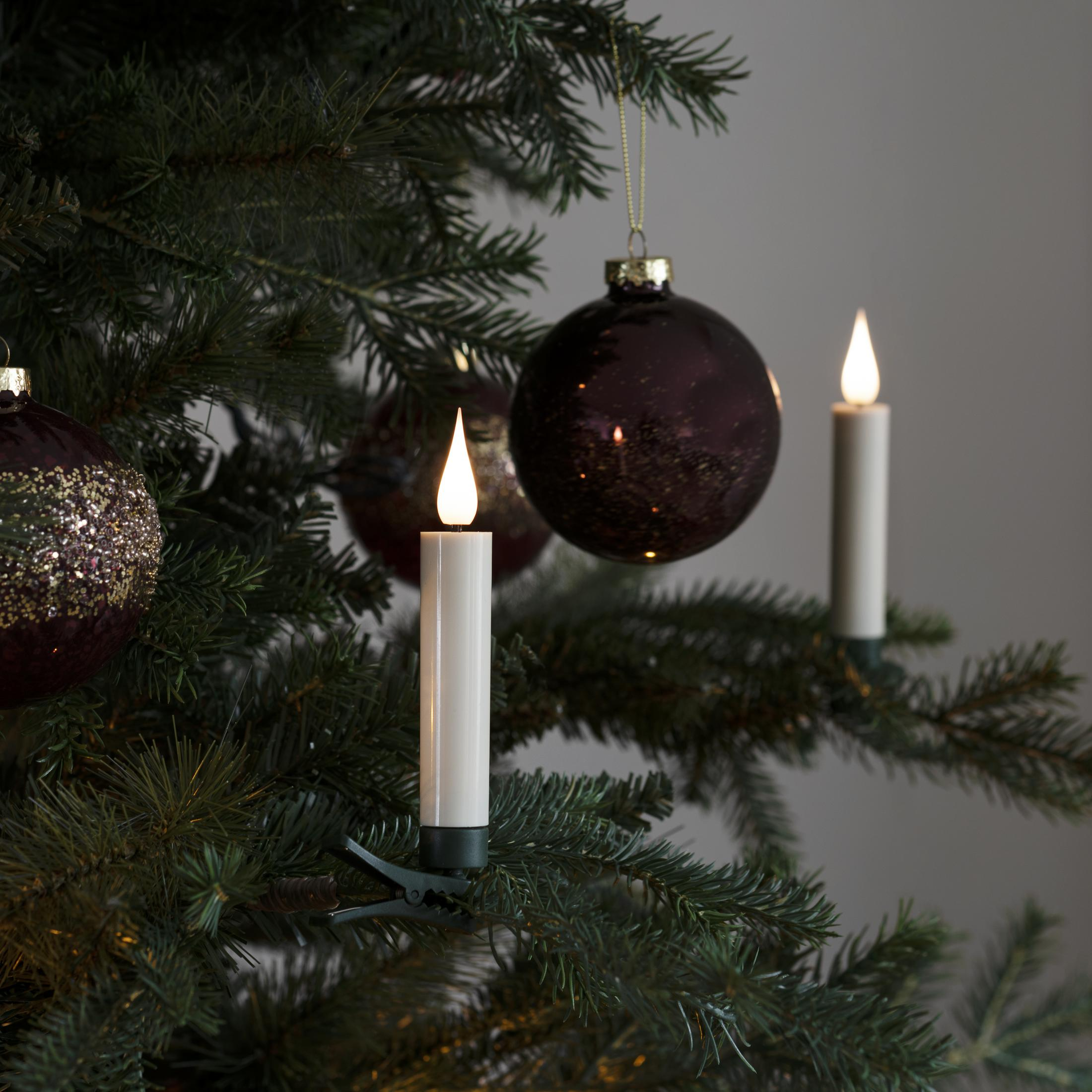 Albero di Natale con ornamenti, candele accese e palline viola scuro.
