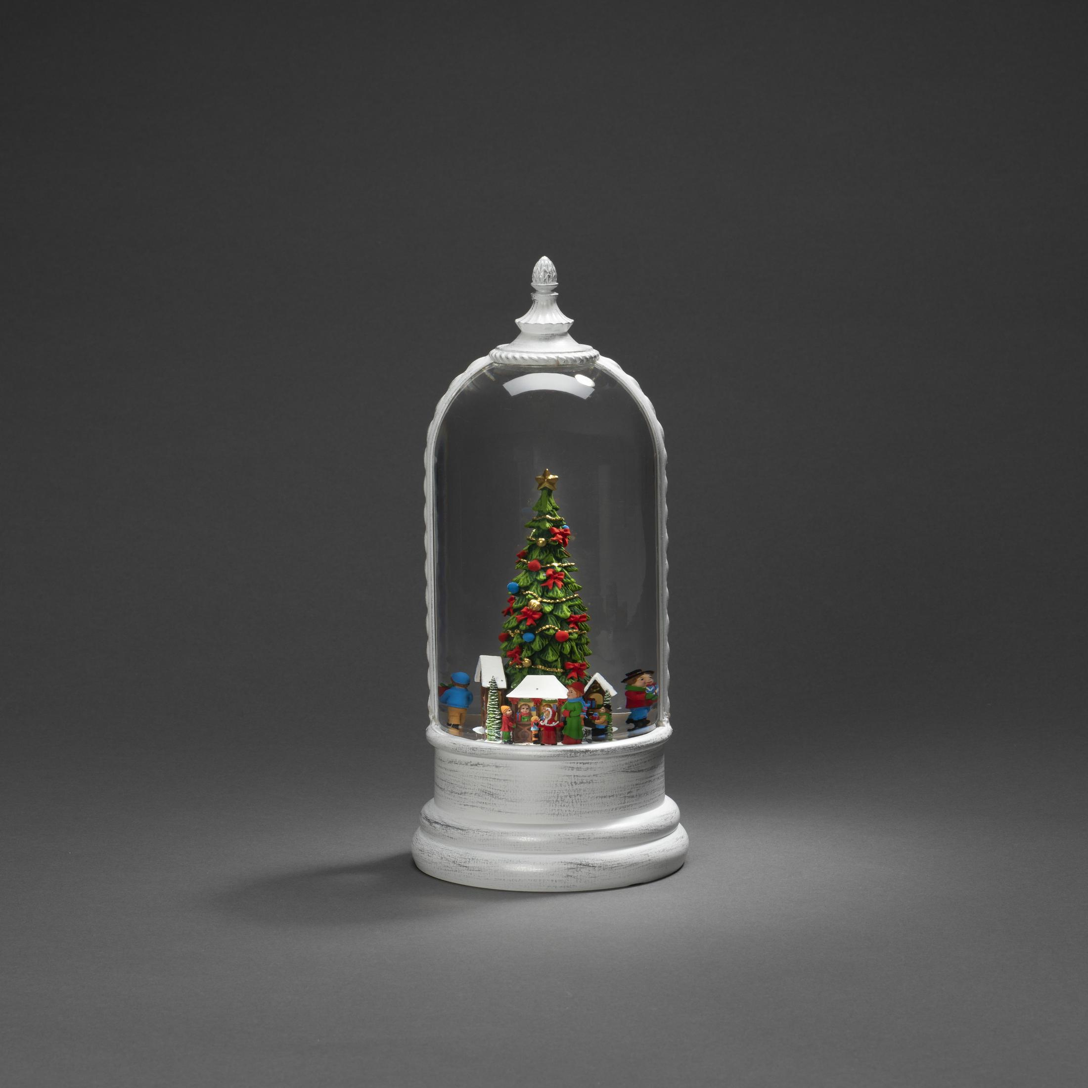 Eine Schneekugel mit einem Weihnachtsbaum, Miniaturhäusern und Figuren, auf einem weißen Sockel.