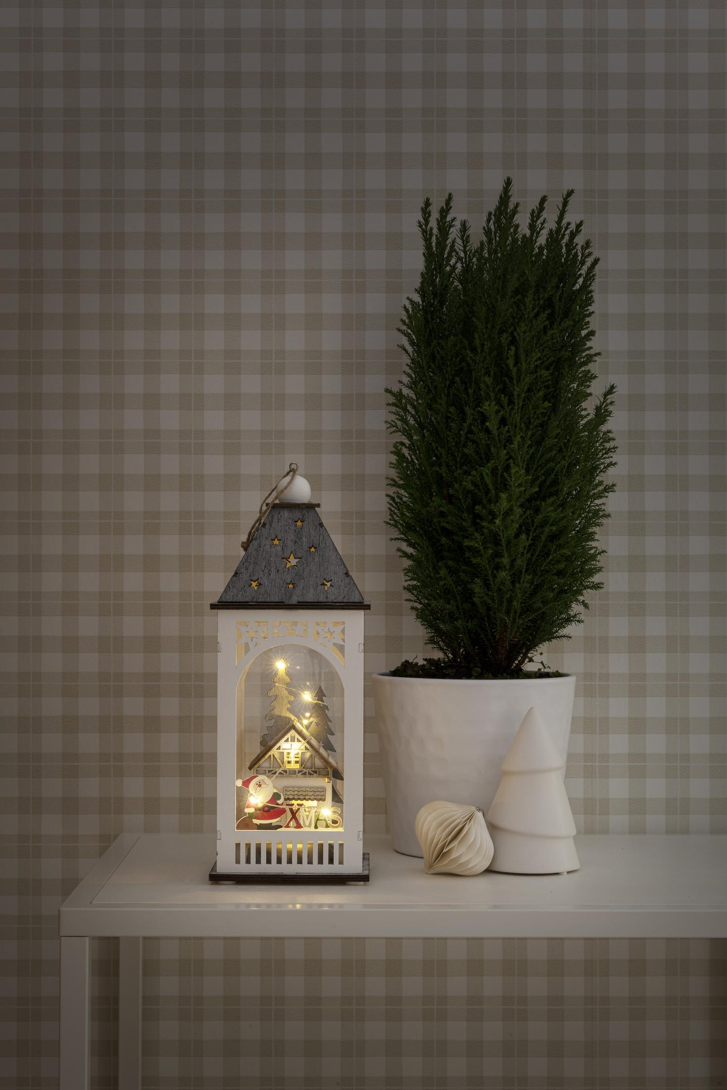 Eine Weihnachtslaterne mit Lichtern, ein kleiner Baum und ein weißer Baumschmuck.