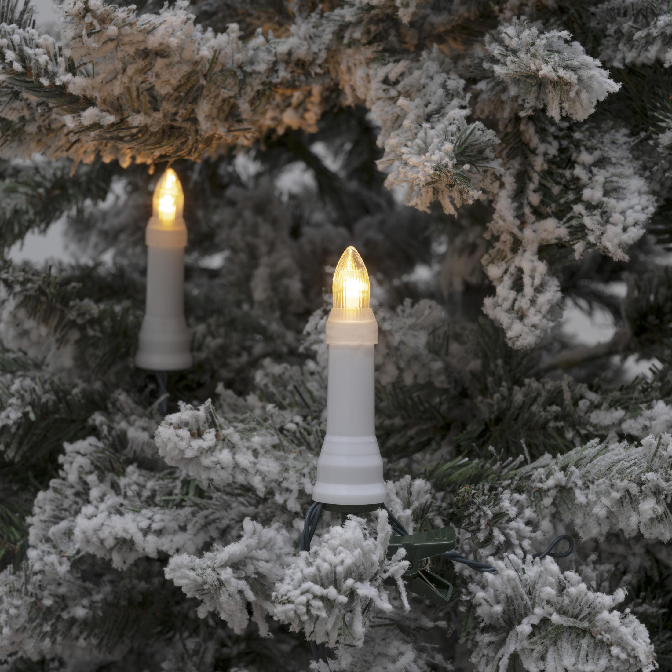 Zwei kerzenförmige Lichter an einem schneebedeckten Weihnachtsbaum. Die Lichter sind weiß mit gelben Glühbirnen.