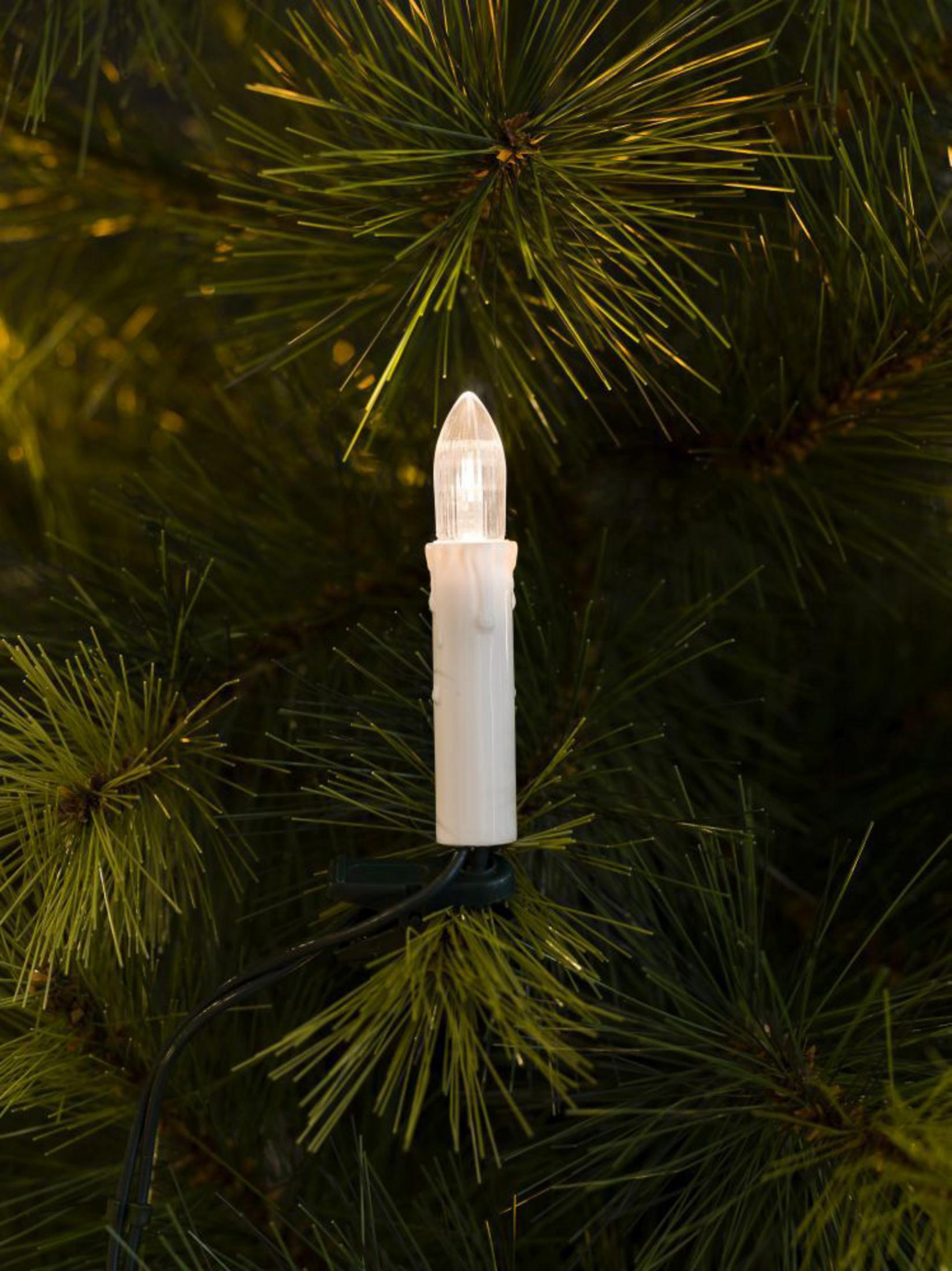 Ein weißes, kerzenförmiges Weihnachtsbaumlicht auf grünen Nadeln.