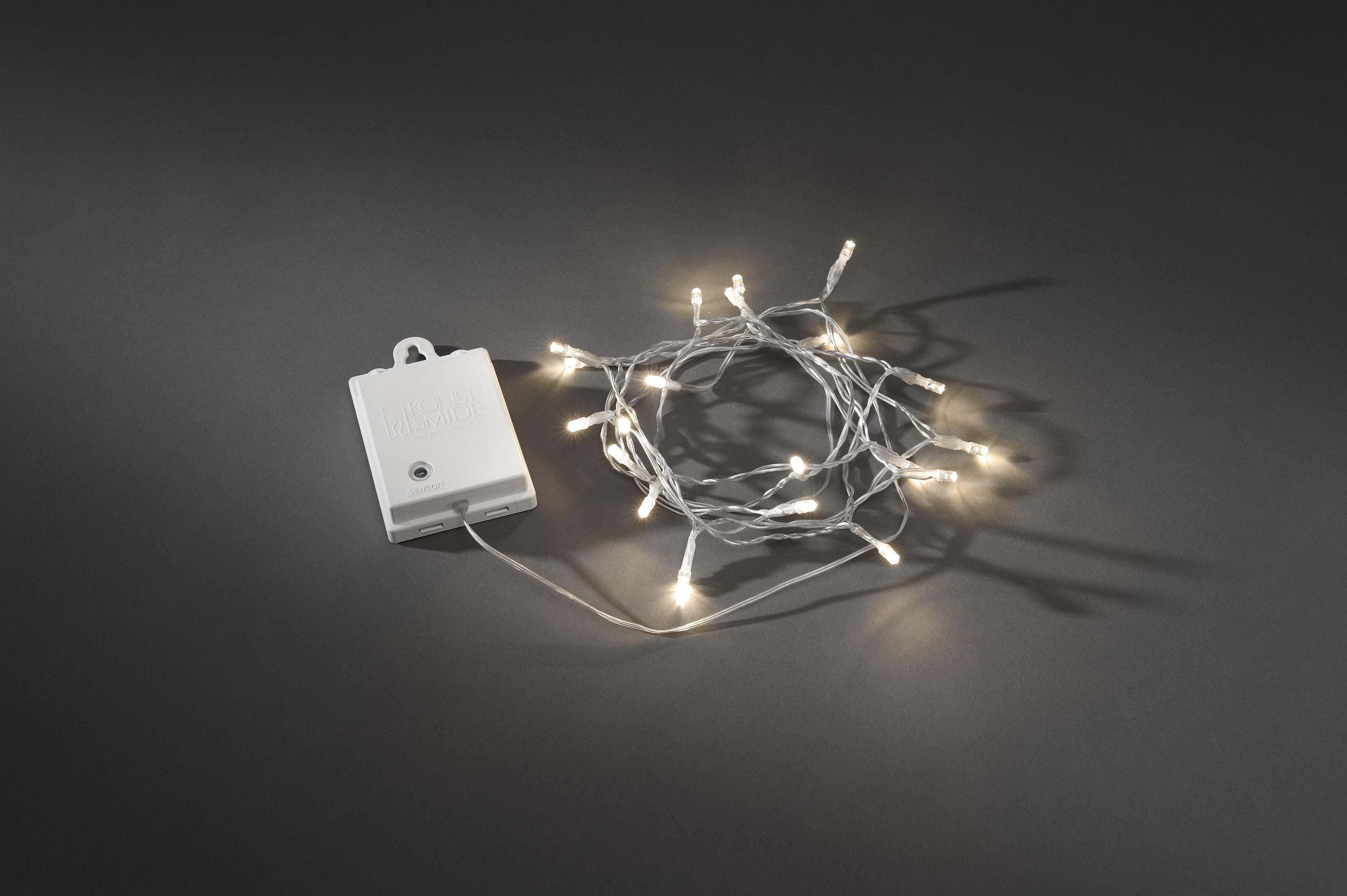 Weiße LED-Lichterkette mit weißem Akku auf grauem Hintergrund.