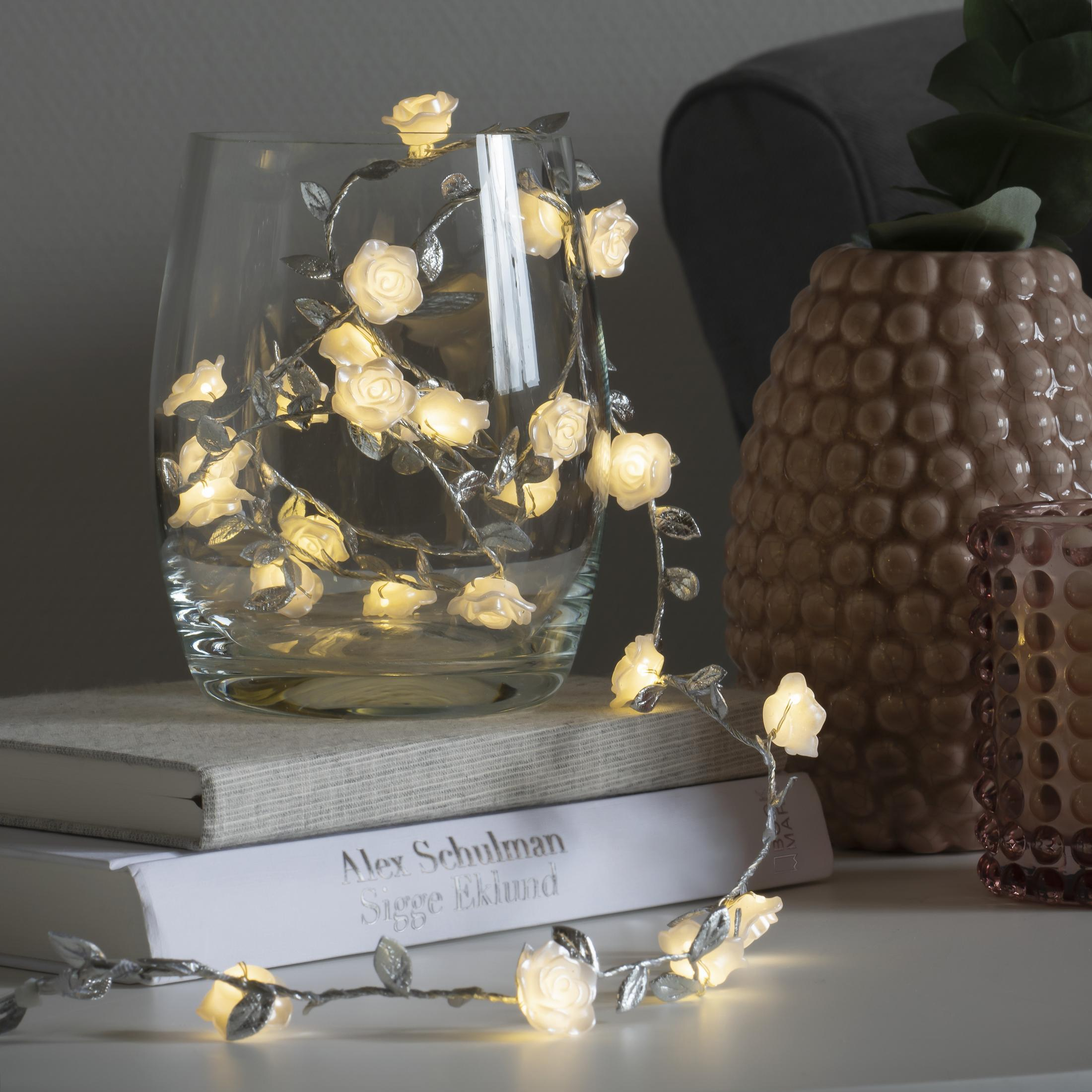 Glasvase mit Rosenlichtern auf einem Buch und einer dunklen Vase.