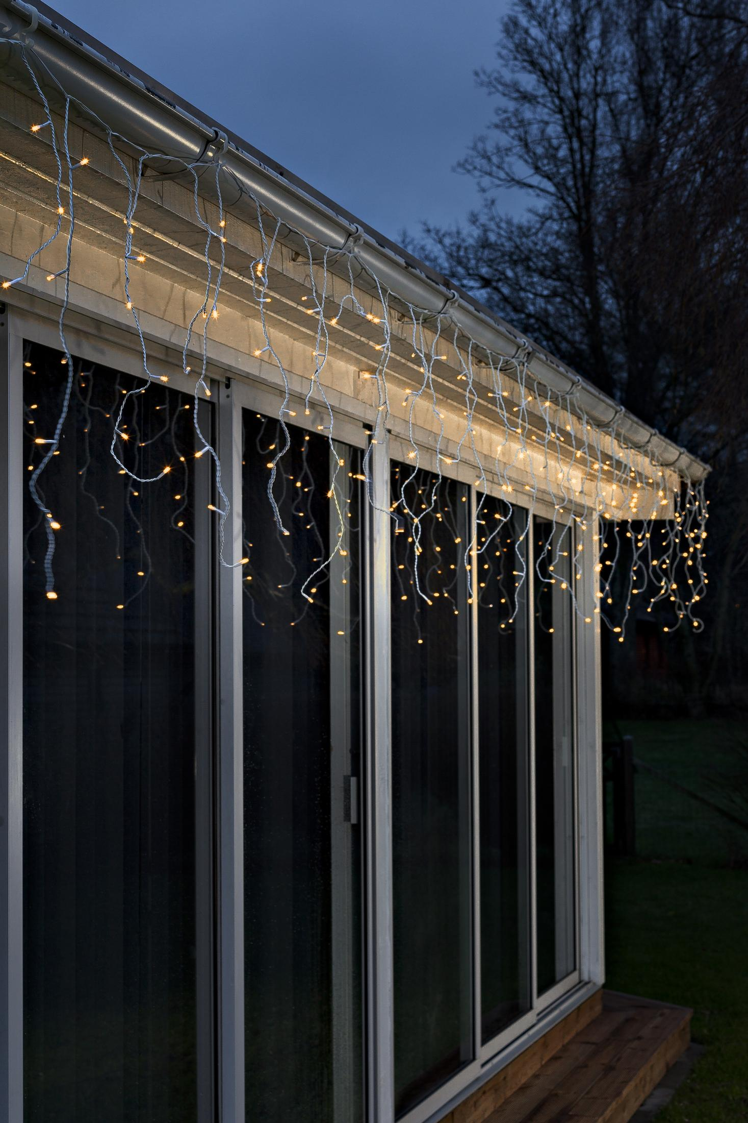Weihnachtslichter an einem weißen Dach, die vor dunklem Hintergrund herunterhängen.