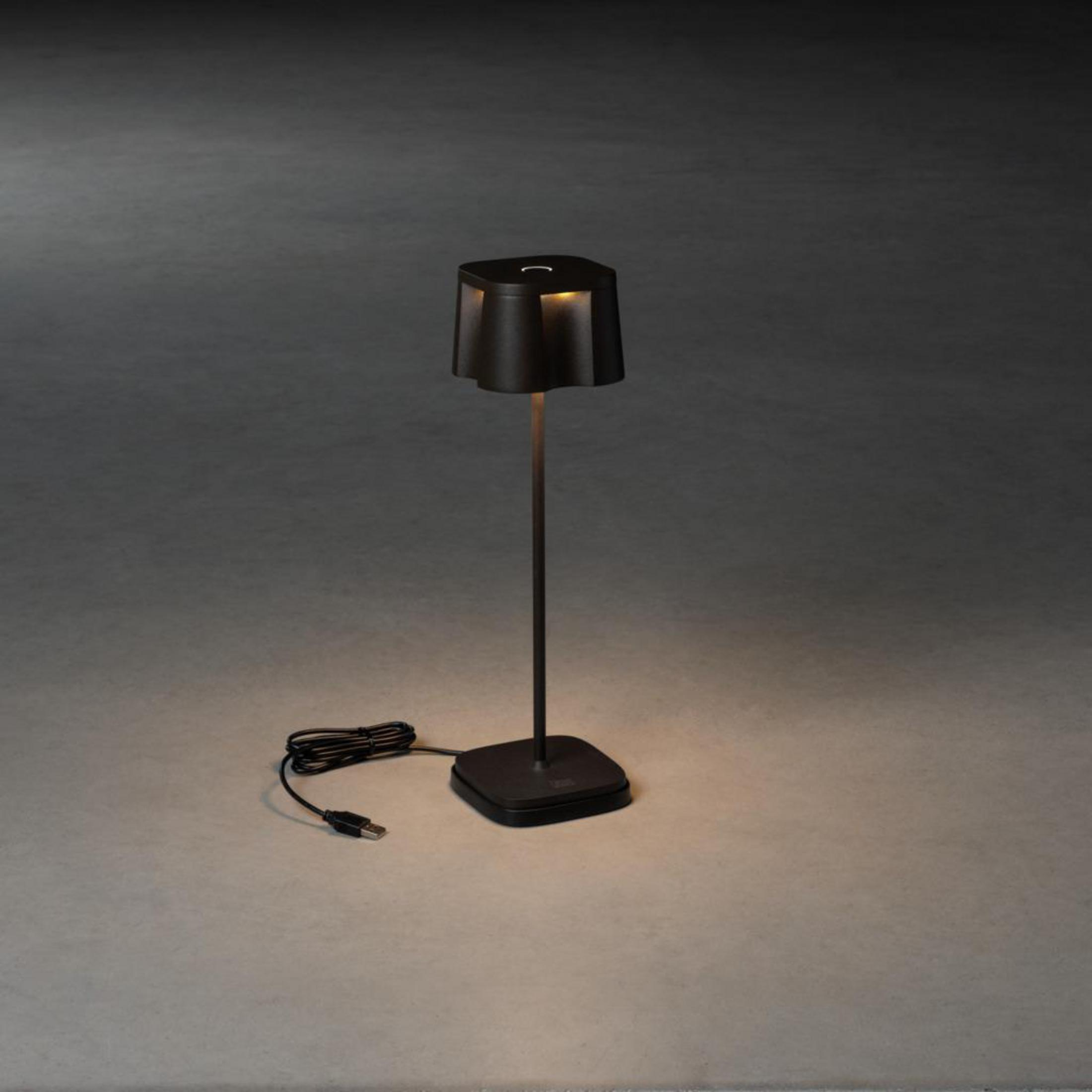 Eine moderne schwarze Lampe mit quadratischem Sockel und langem Schaft, angeschlossen an eine Steckdose.