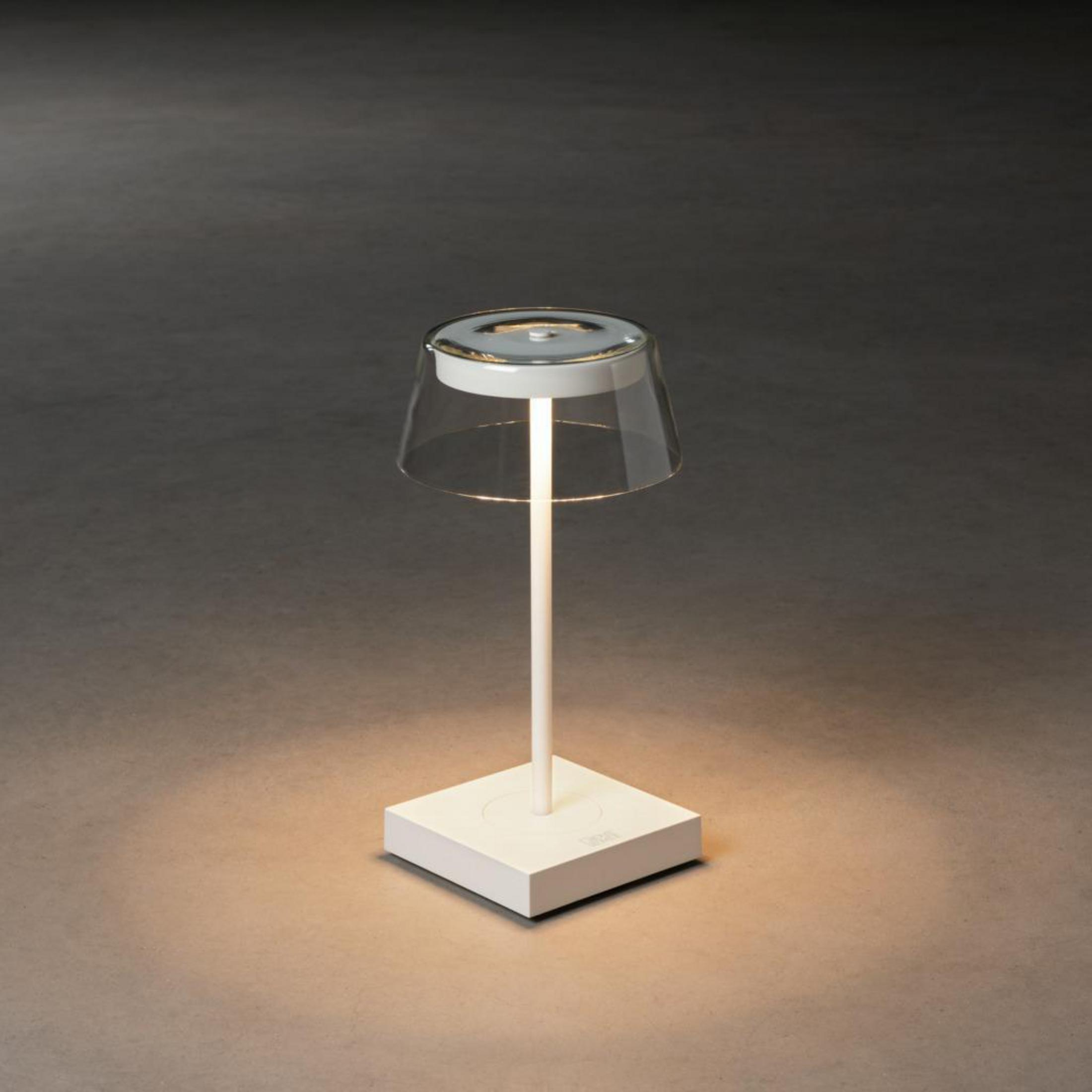 Lampada da comodino bianca con paralume trasparente, su base quadrata.