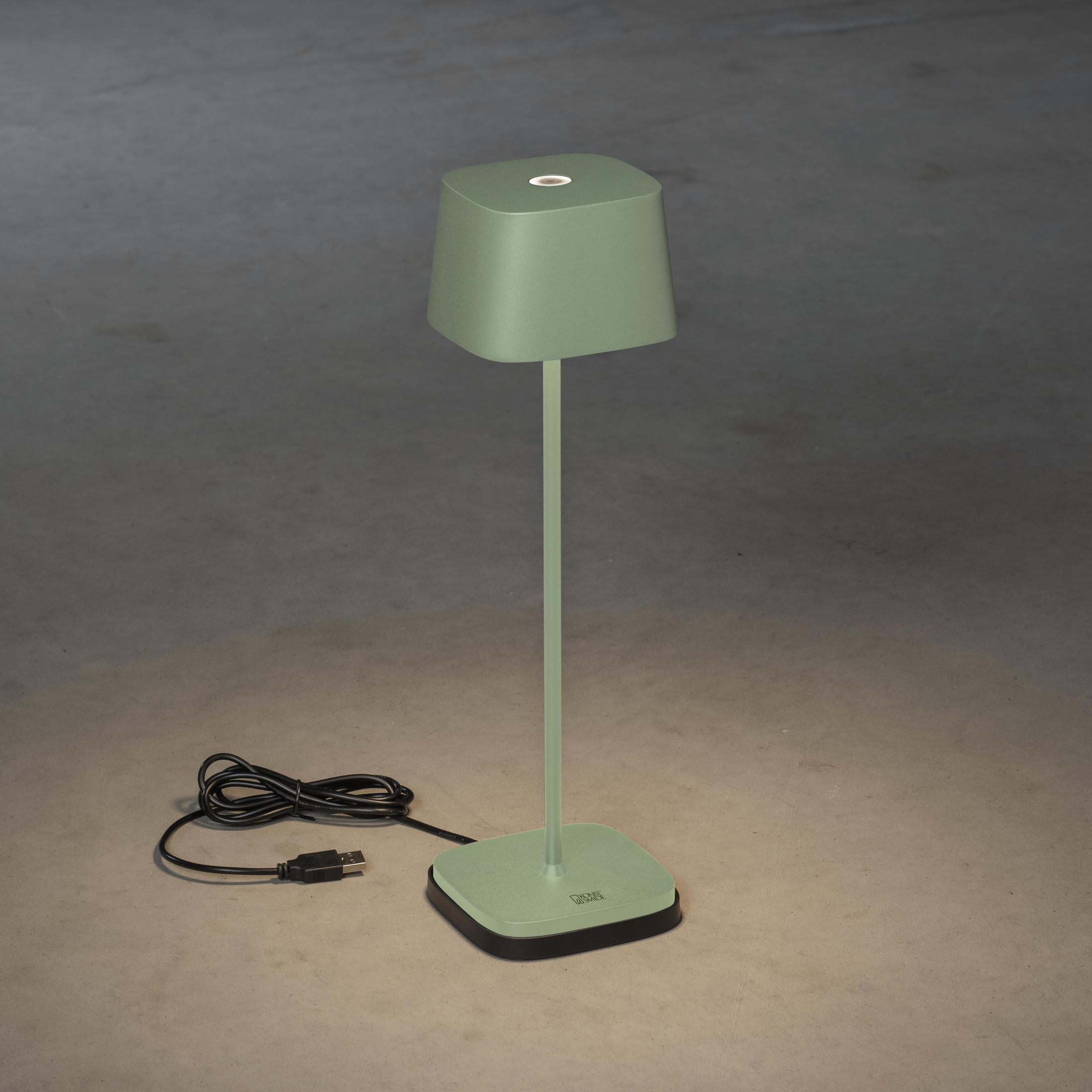 Grüne Tischlampe mit quadratischem Sockel und Schirm. Sie steht auf grauem Untergrund. Schwarzes Kabel sichtbar.
