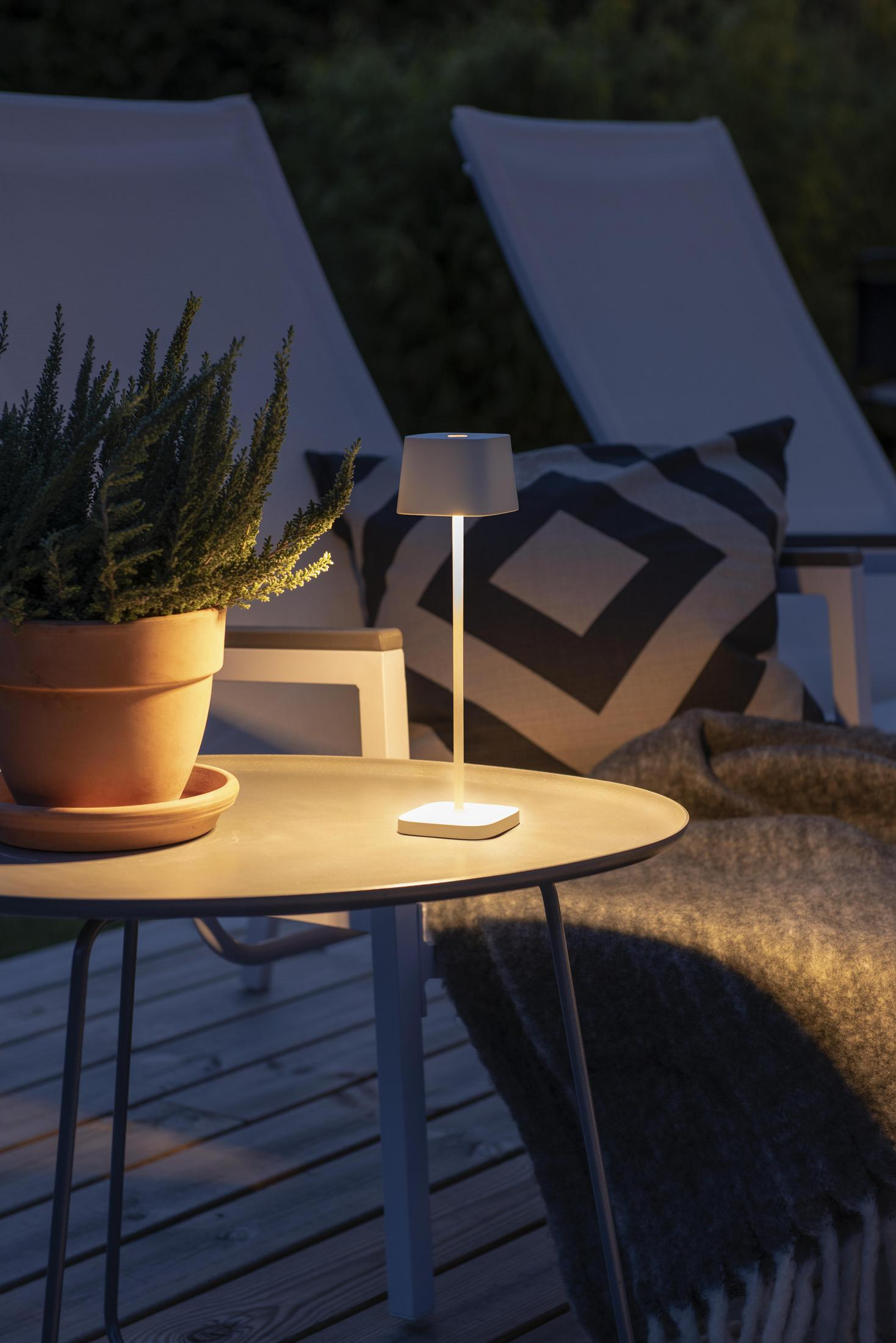 Zapalone lampa stołowa na stole w ogrodzie o zmierzchu, z krzesłami.