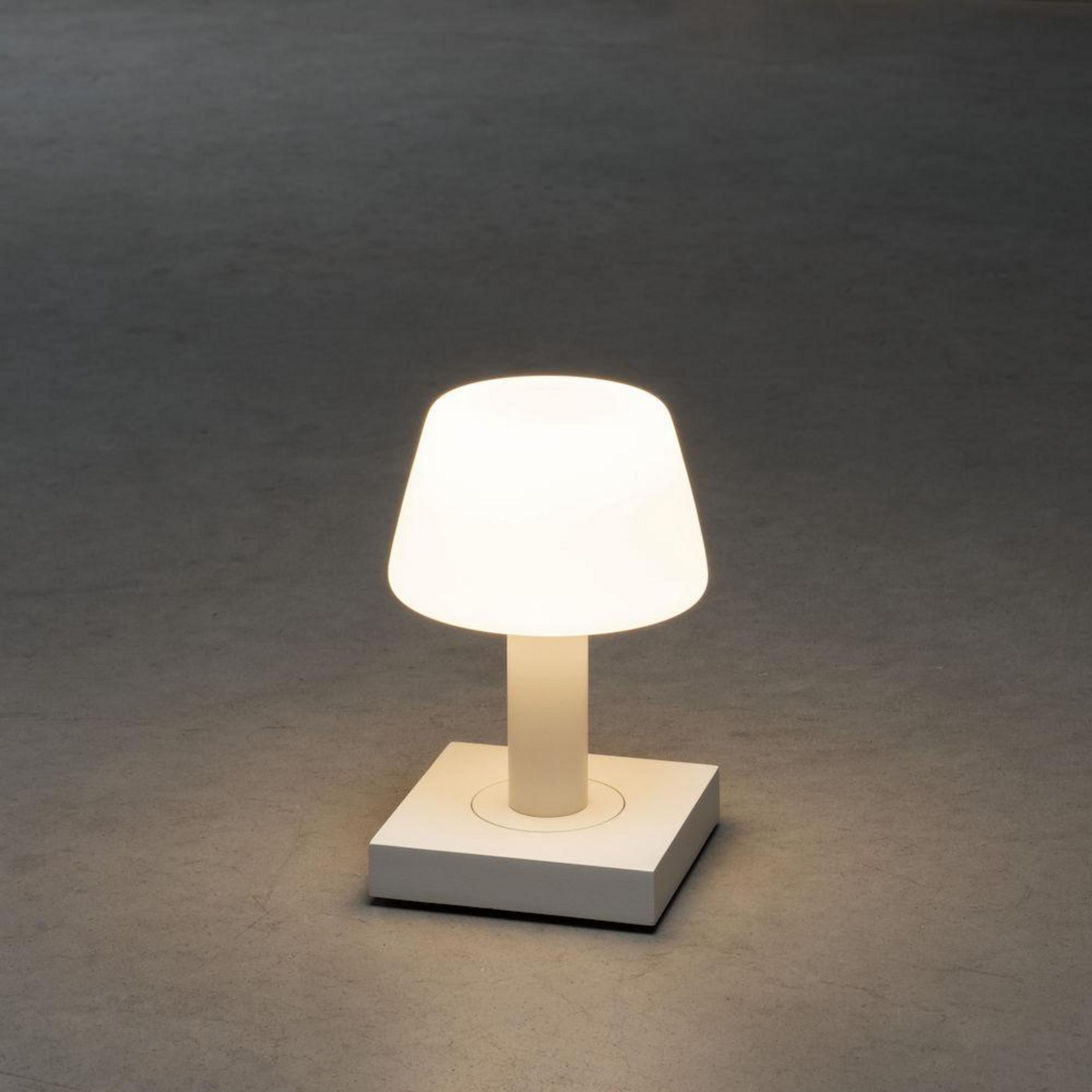 Weiße Lampe mit quadratischem Sockel. Die Lampe ist beleuchtet, der Hintergrund ist grau.