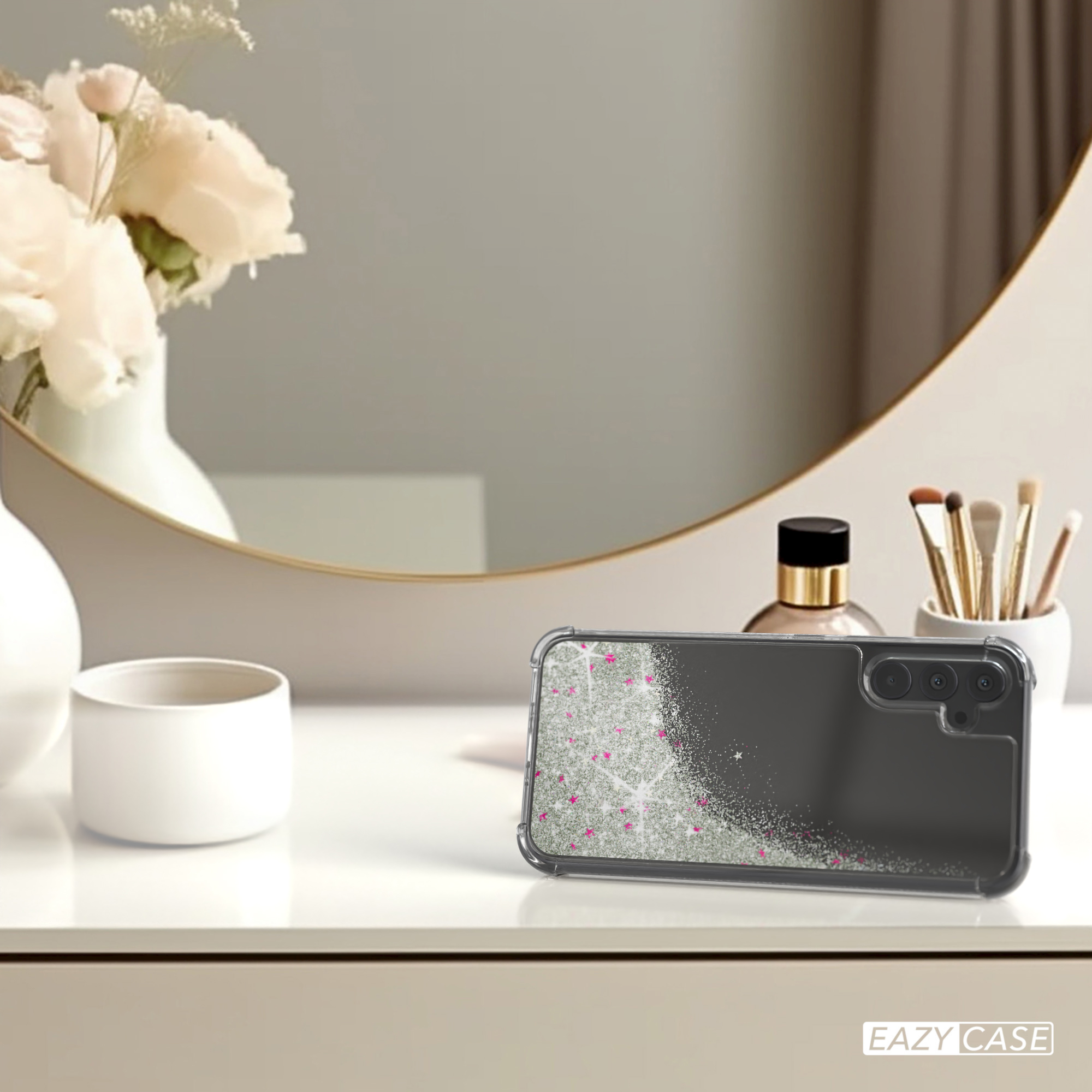 Handyhülle auf einem Tisch mit Blumen, Spiegel und Make-up-Artikeln. Klare Hülle mit rosa Glitzer.