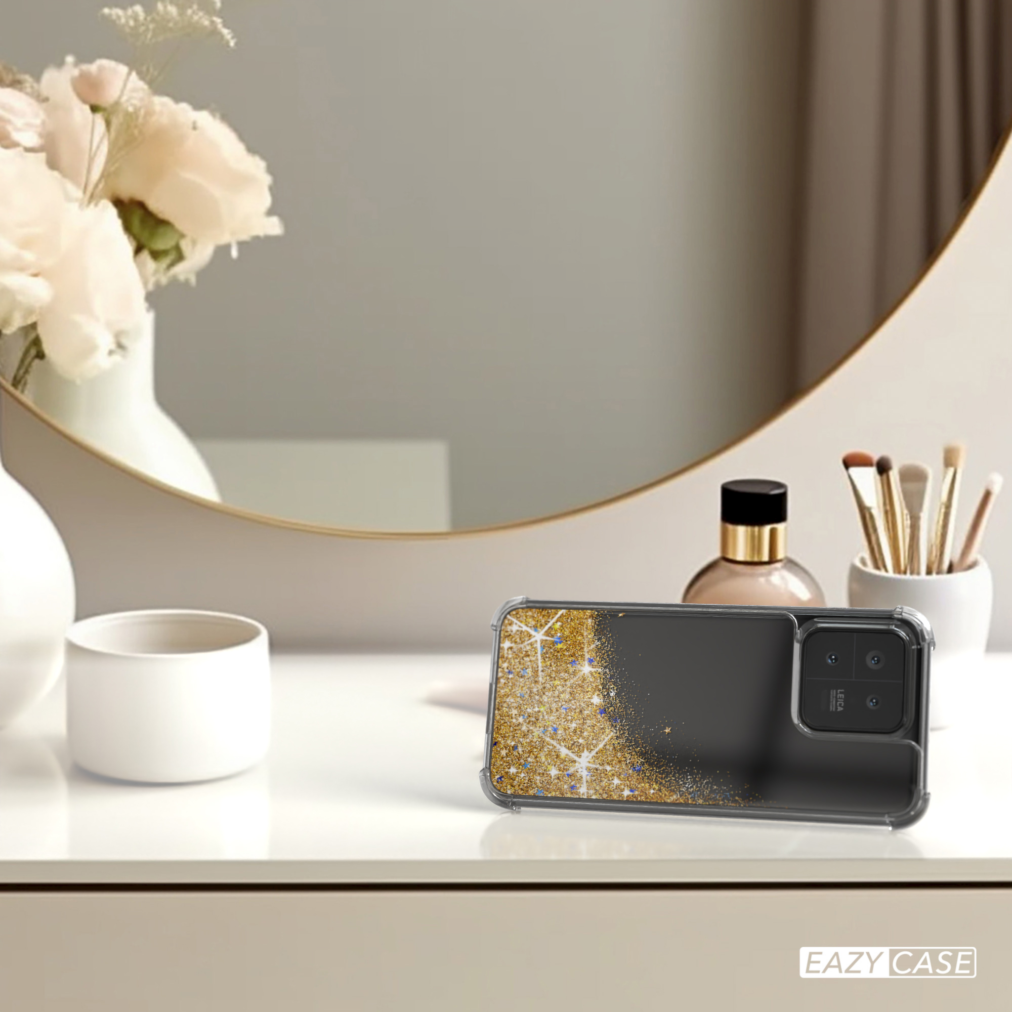 Handyhülle mit Goldglitzer-Design auf einem Schreibtisch mit Make-up und Spiegel im Hintergrund.