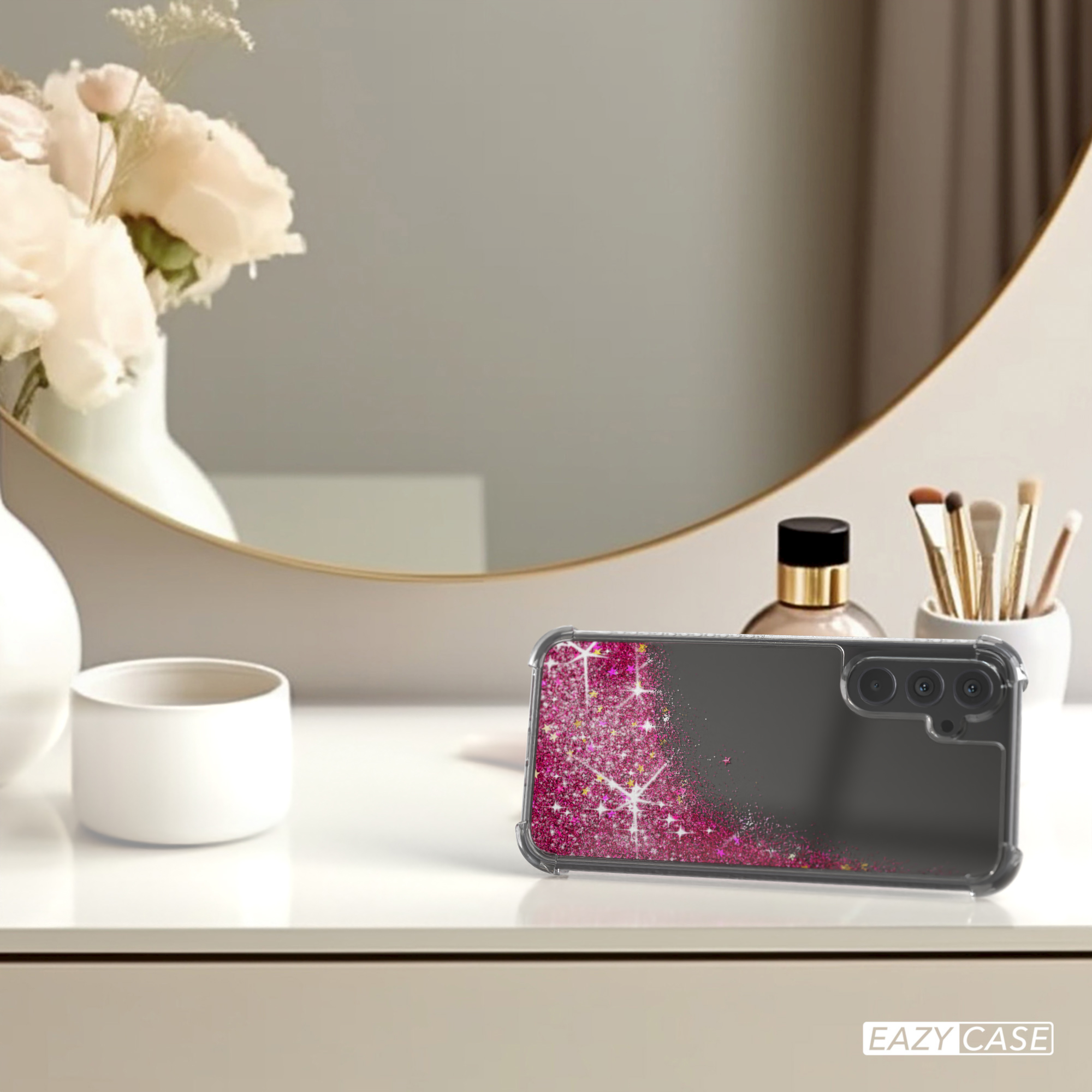 Handyhülle mit rosa Glitzer auf einem weißen Tisch neben Spiegel und Kosmetikartikeln.