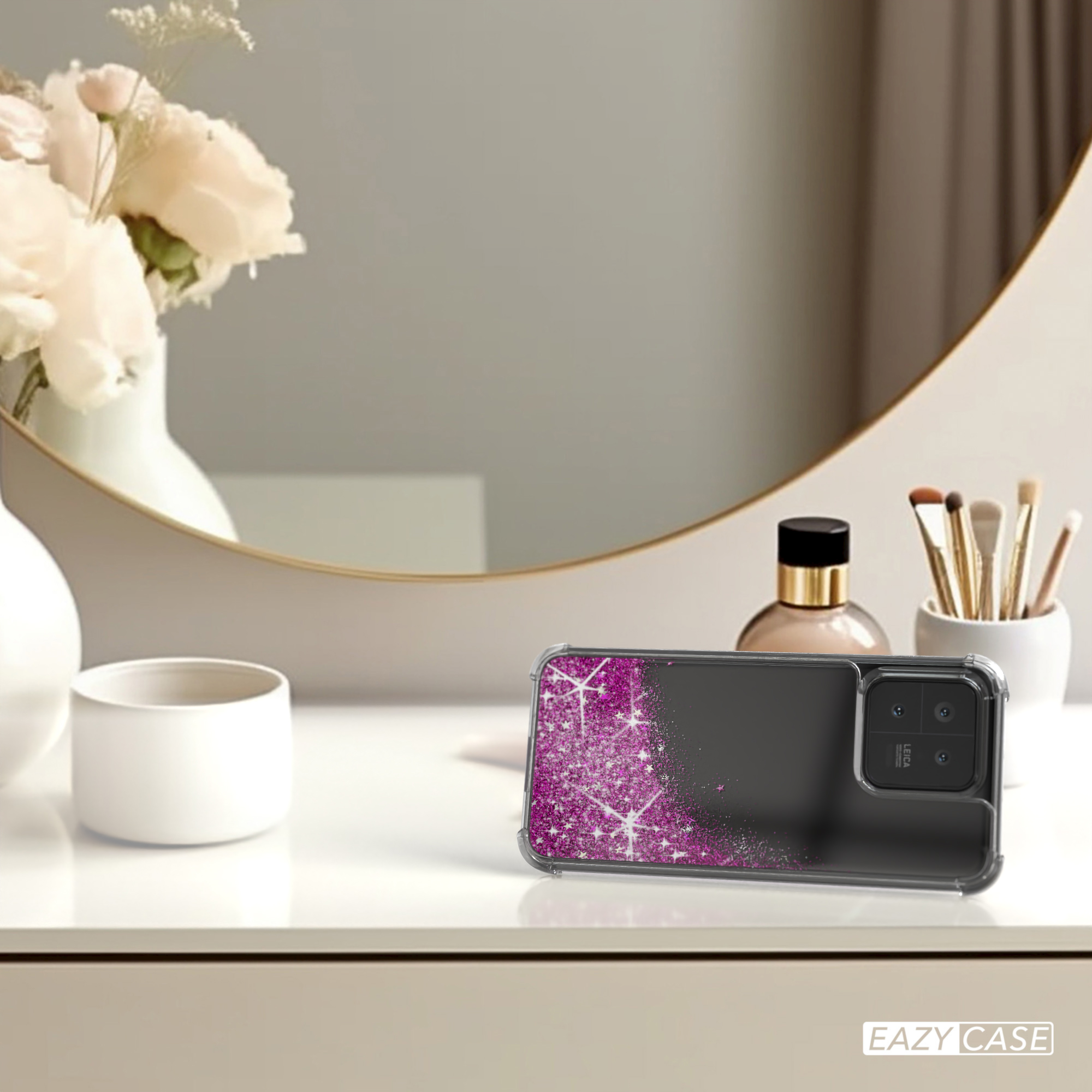 Eine Handyhülle mit rosa Glitzer auf einem Tisch, in der Nähe eines Spiegels und Schönheitsprodukten.