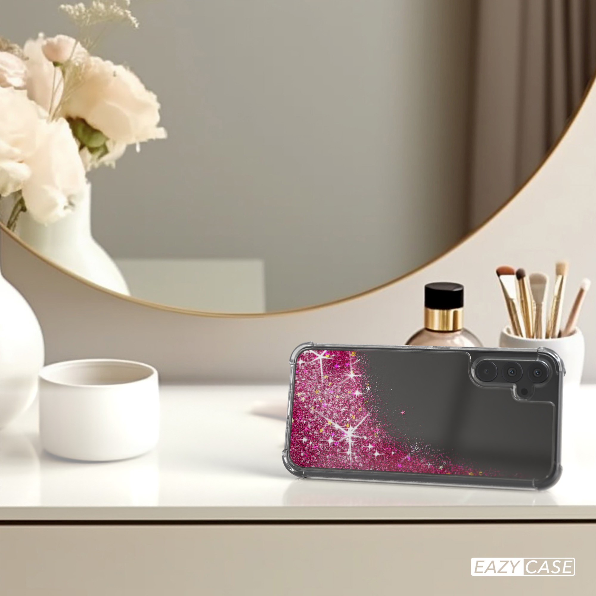 Eine Handyhülle mit Glitzer liegt auf einem Tisch in der Nähe eines Spiegels, einer Vase und Make-up-Pinseln.