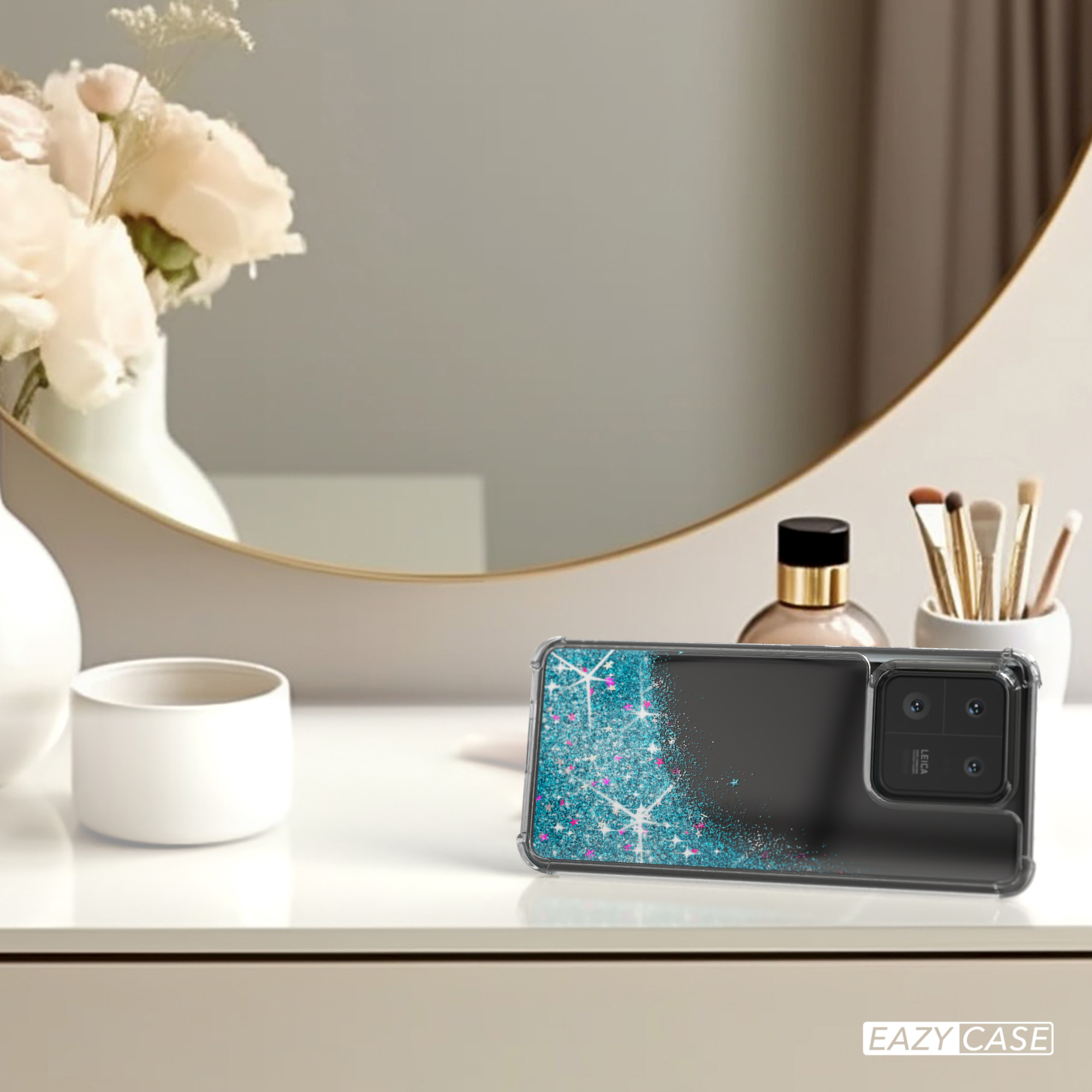 Ein Telefon mit Glitzerhülle auf einem Tisch mit Blumen und Spiegel.