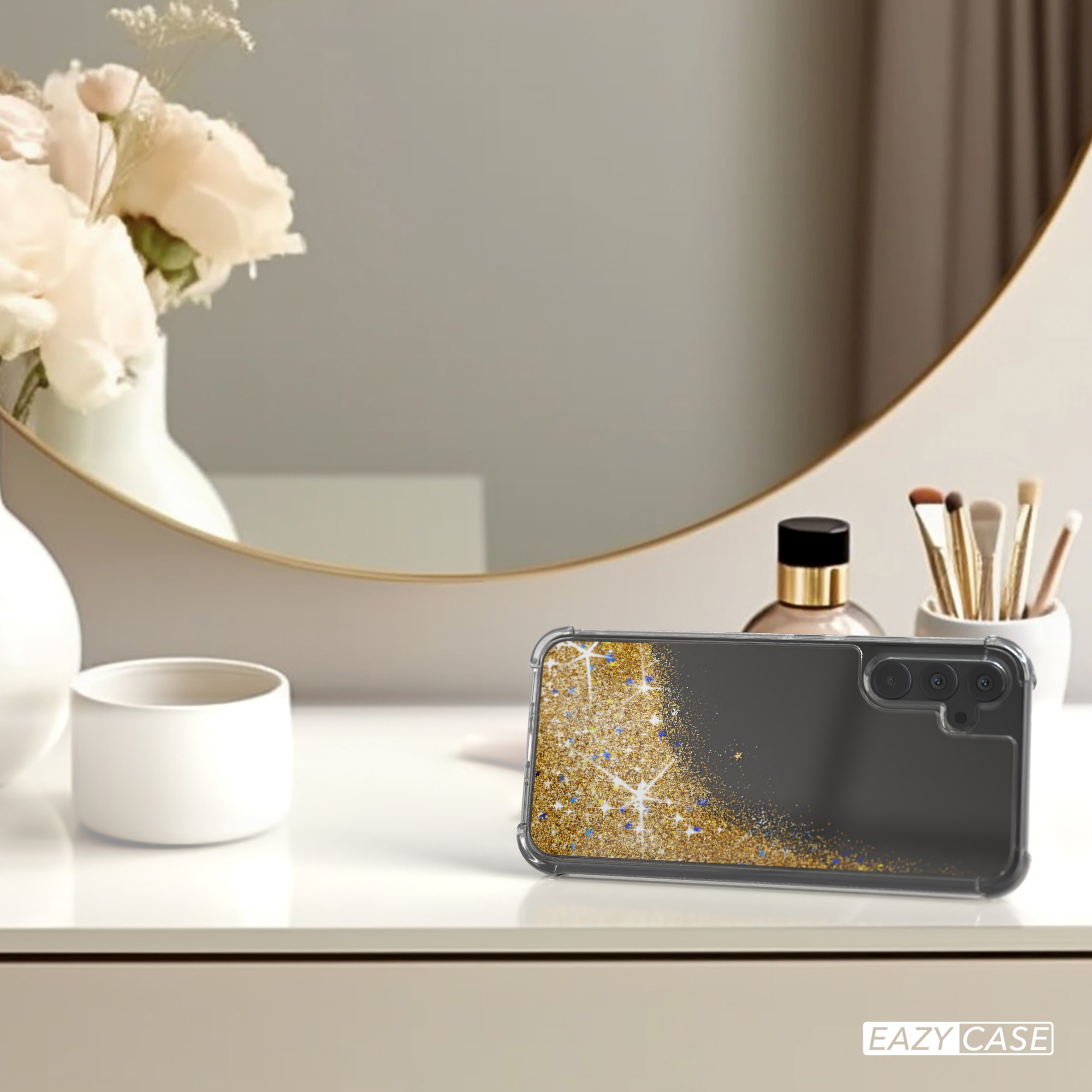 Eine Handyhülle auf einem Tisch mit Spiegel, Blumen und Make-up. Hülle hat goldenes Design.