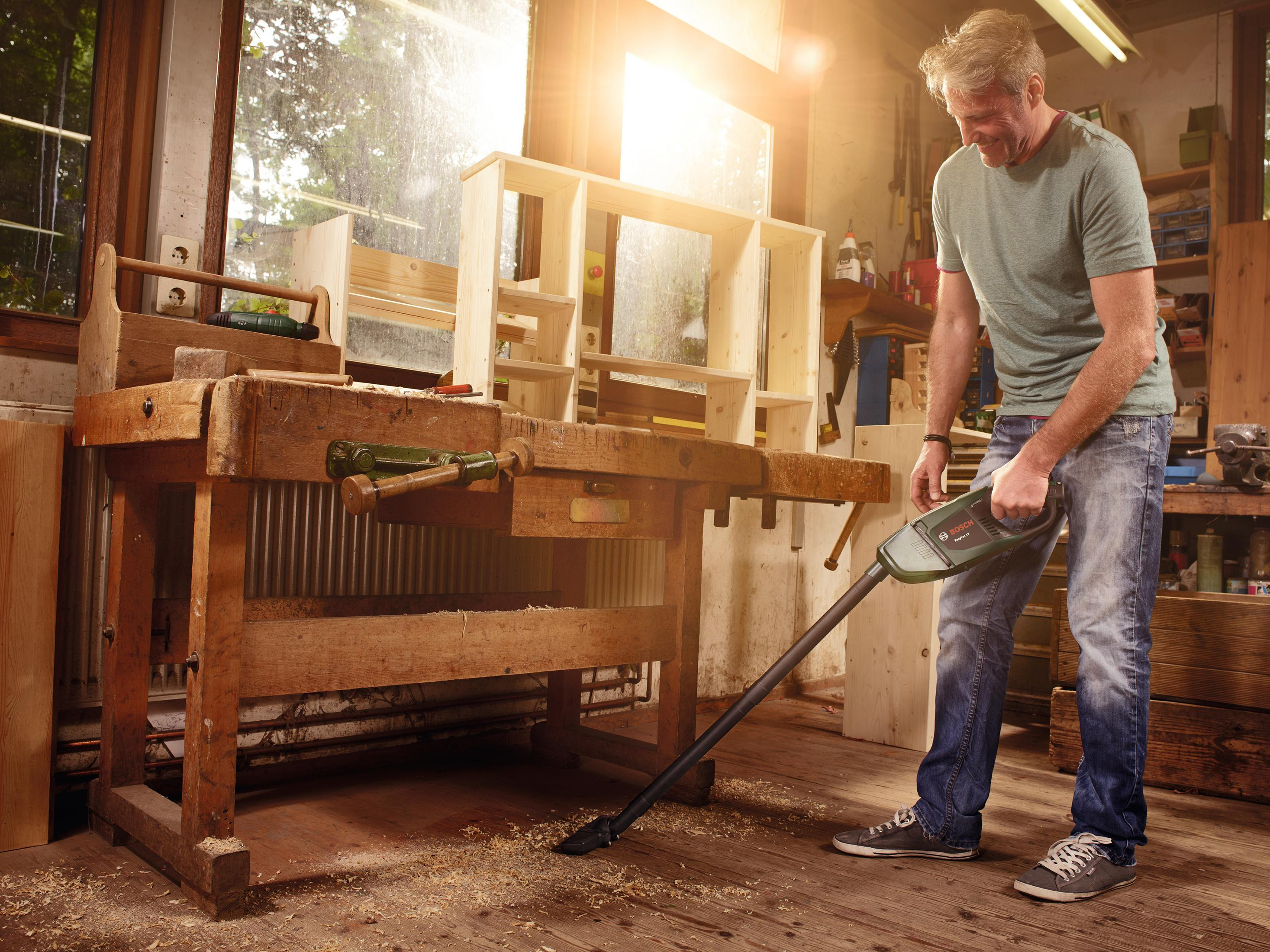Homme utilisant un aspirateur dans un atelier. Soleil brille à travers la fenêtre.