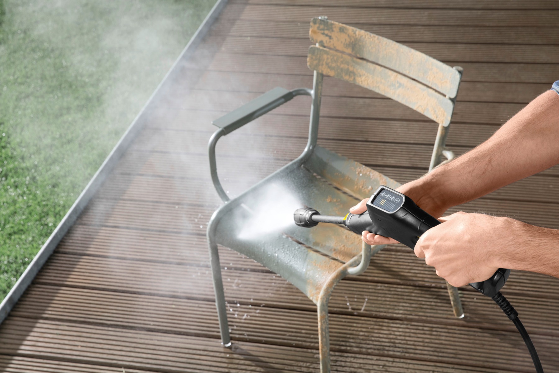 Eine Person reinigt einen rostigen Metallstuhl mit einem Hochdruckreiniger auf einem Holzdeck.