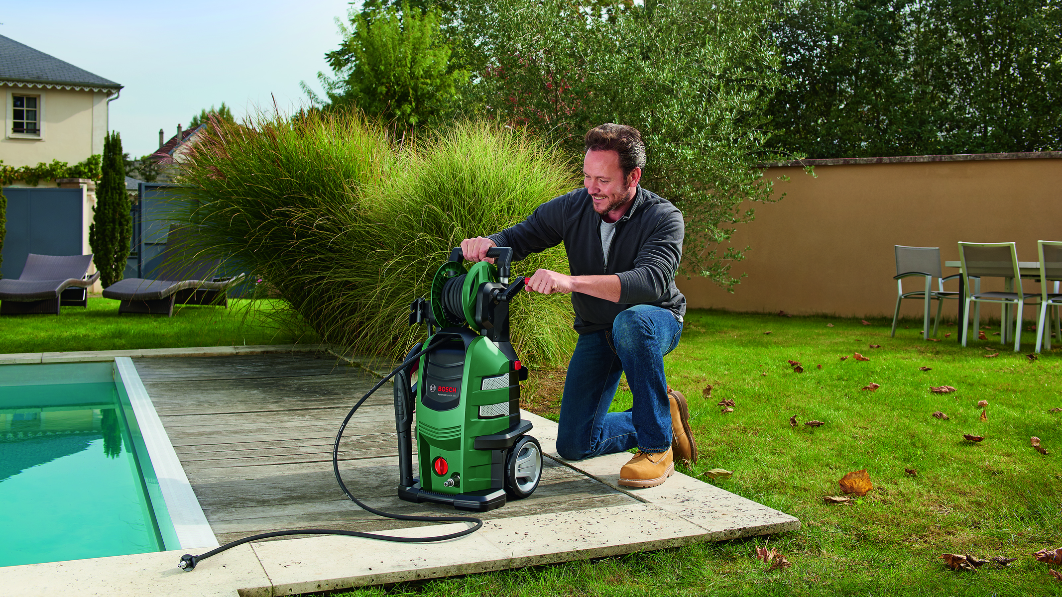 Homme utilisant un nettoyeur haute pression sur un patio. Le nettoyeur est vert et noir. Jour ensoleillé.