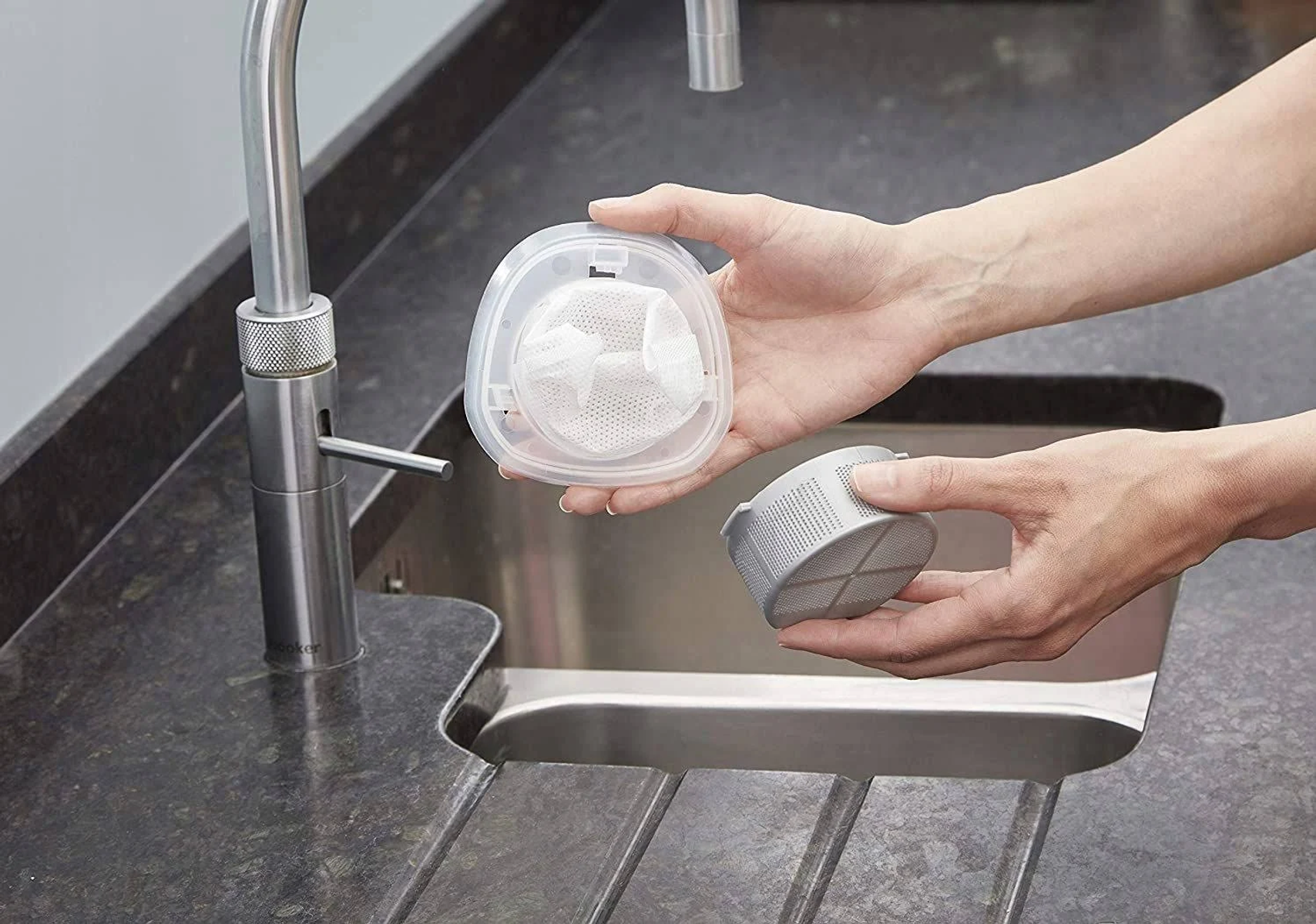 Dłonie trzymające i montujące filtr do kranu zlewozmywakowego.