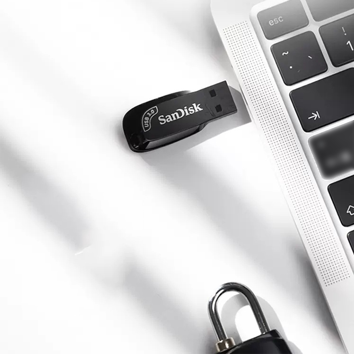 Ein schwarzer SanDisk USB-Stick neben einer Laptop-Tastatur und einem Vorhängeschloss.