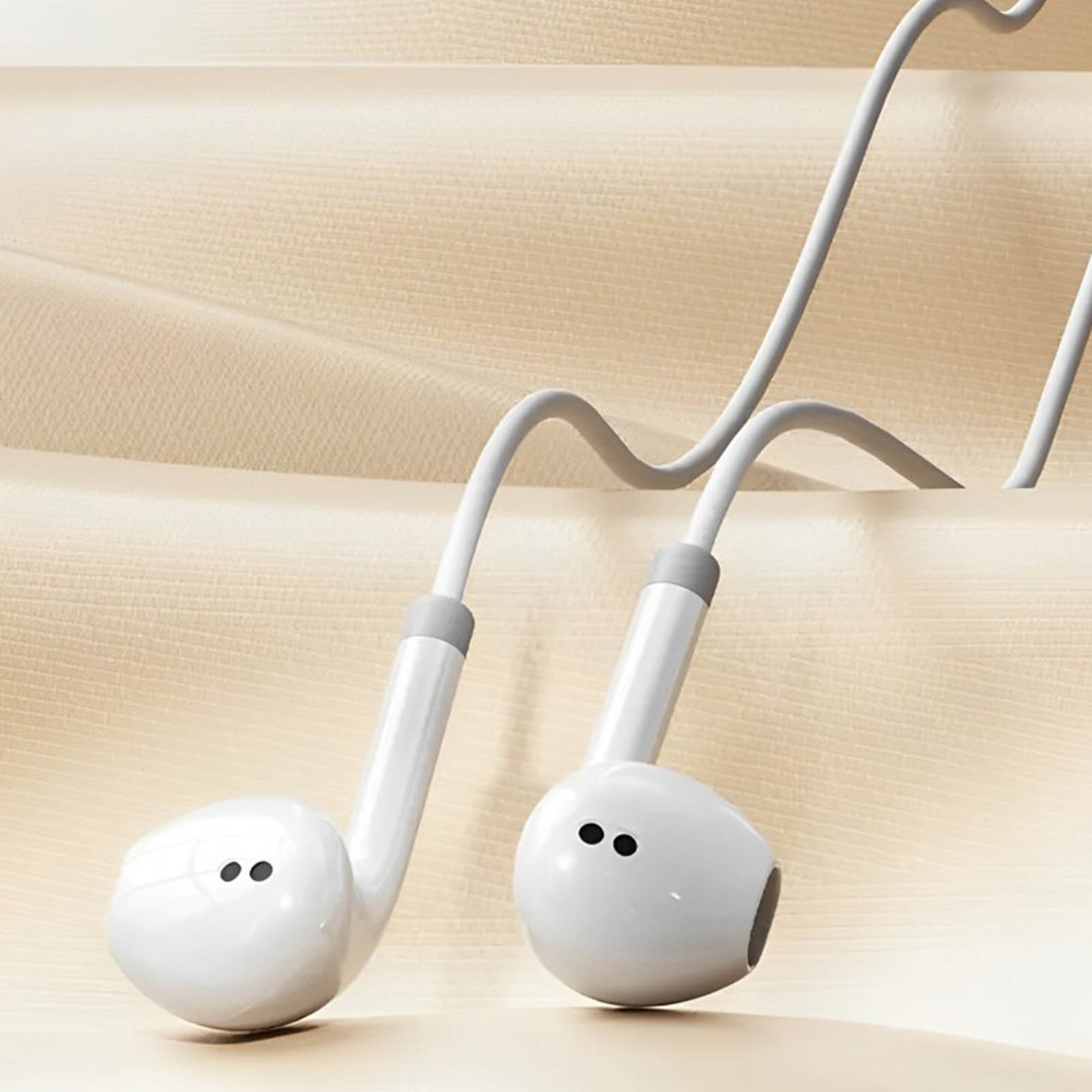 Weiße Ohrhörer mit grauem Kabel vor beige-hellbraunem Hintergrund.
