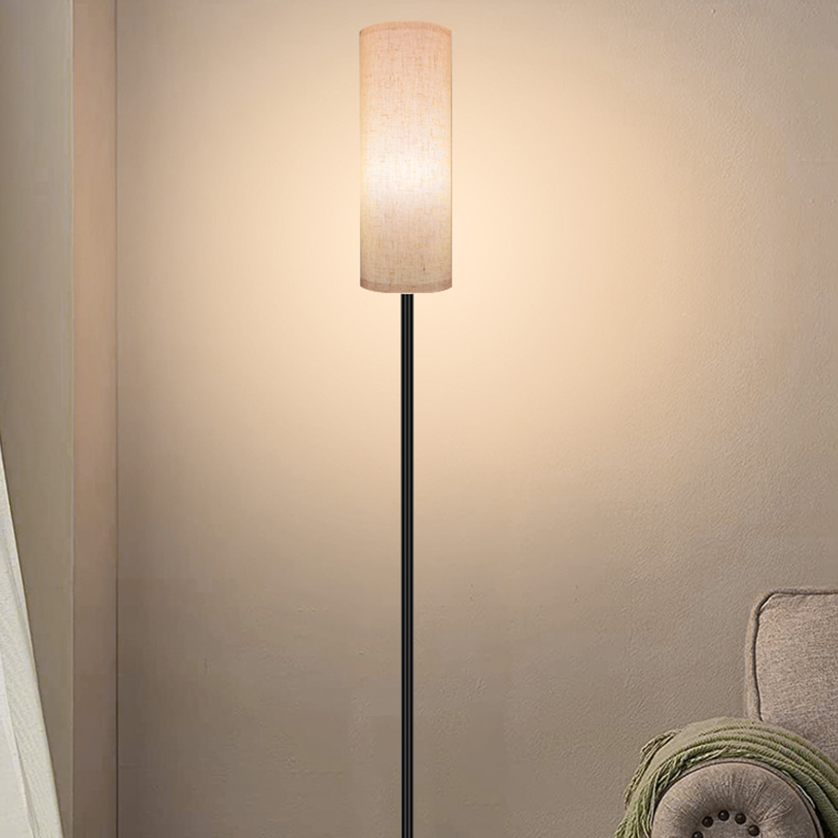 Eine hohe, schlanke Stehlampe mit beigem Schirm, die vor einer Wand steht und sanftes Licht erzeugt.