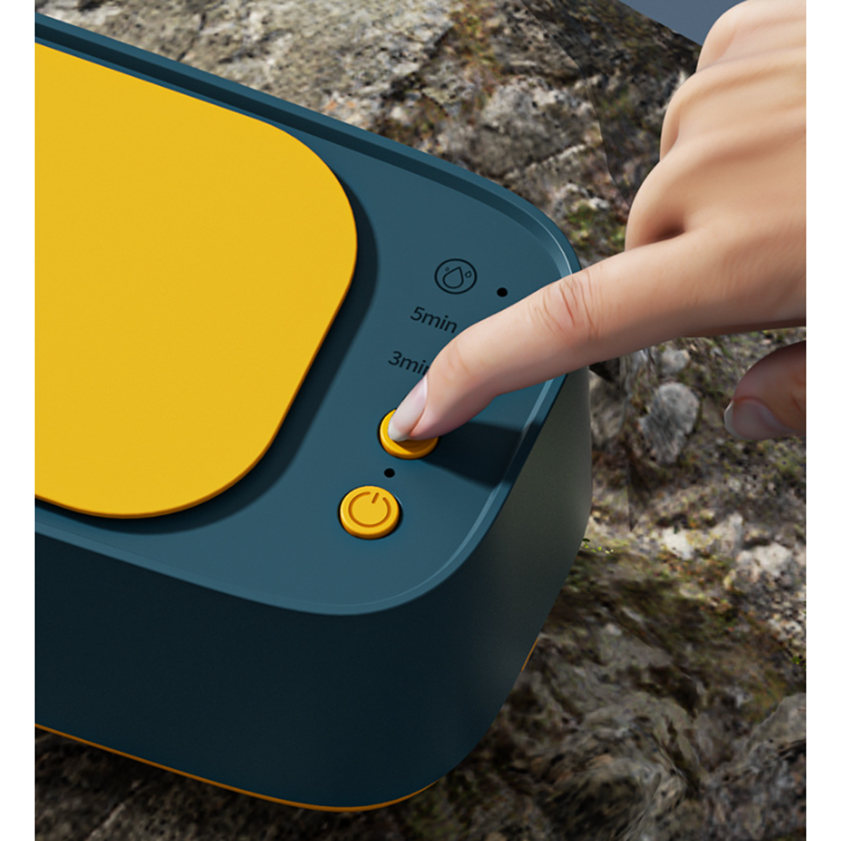 Hand drückt eine Taste auf einem türkis-gelben Gerät, vor einem felsigen Hintergrund.