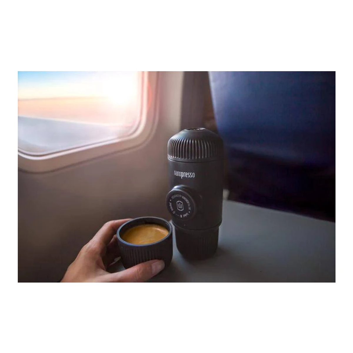 Eine schwarze tragbare Kaffeemaschine mit einer Tasse Kaffee auf einem Tablett. Die Sonne scheint im Hintergrund.